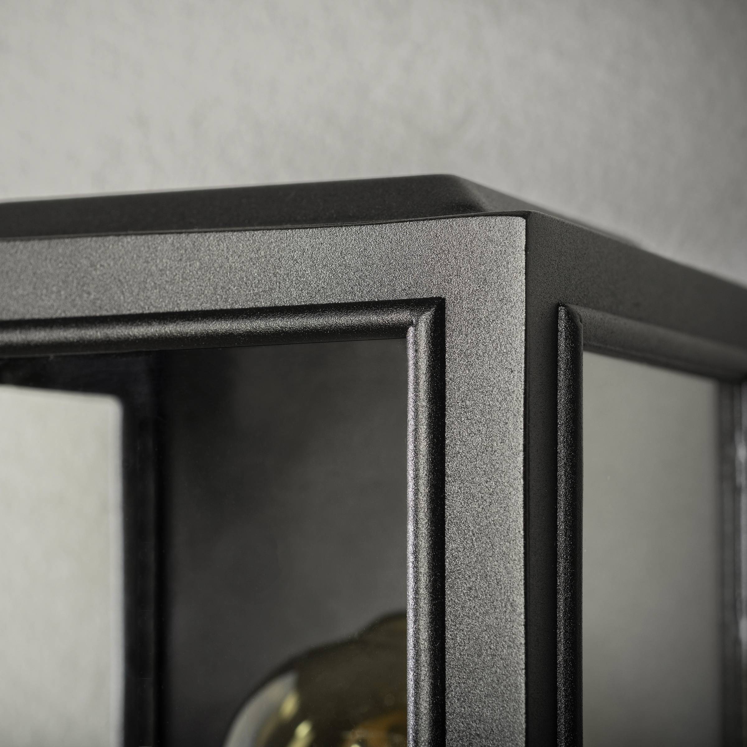 Nahaufnahme einer mattschwarzen Metall-Laterne mit klaren Glasscheiben. Im Inneren ist der obere Teil einer goldenen Glühbirne sichtbar.