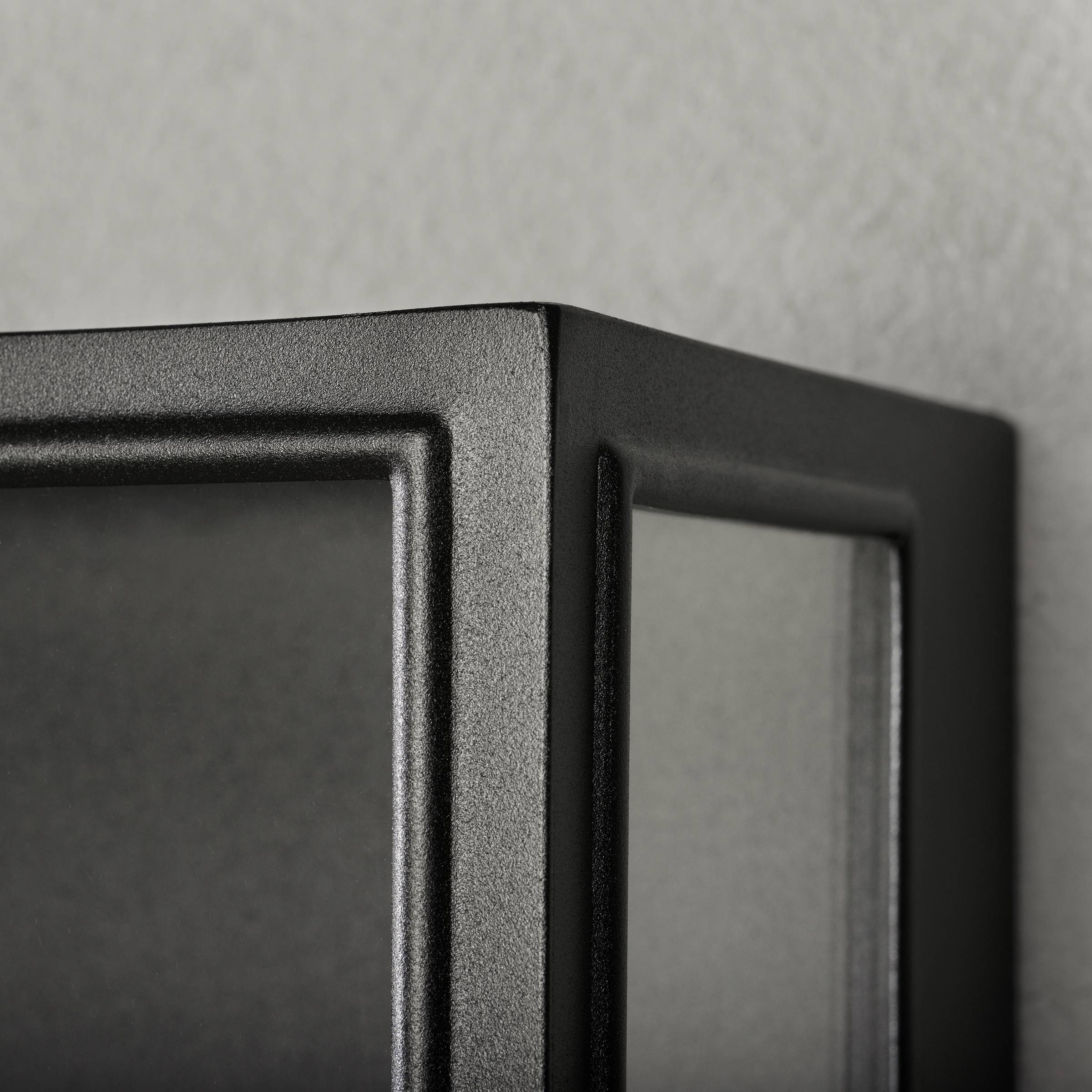 Nahaufnahme eines schwarzen Metallrahmens mit Glas, zeigt glatte Kanten und matte Oberfläche.