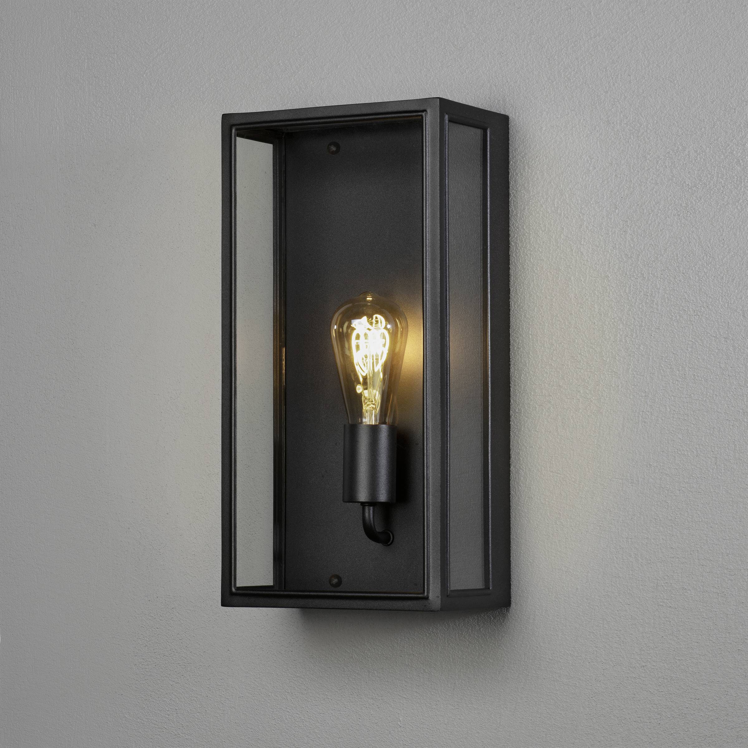 Eine schwarze Wandlampe mit Glühbirne strahlt warmes Licht.