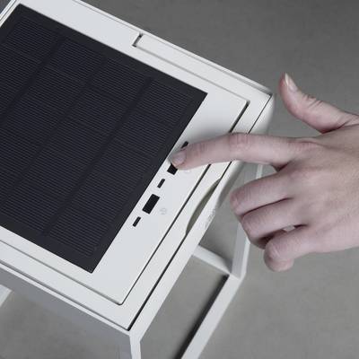 Eine Person bedient ein Gerät mit einem Solarpanel und einem USB-Anschluss. Sie drückt auf einen Knopf neben dem Anschluss.