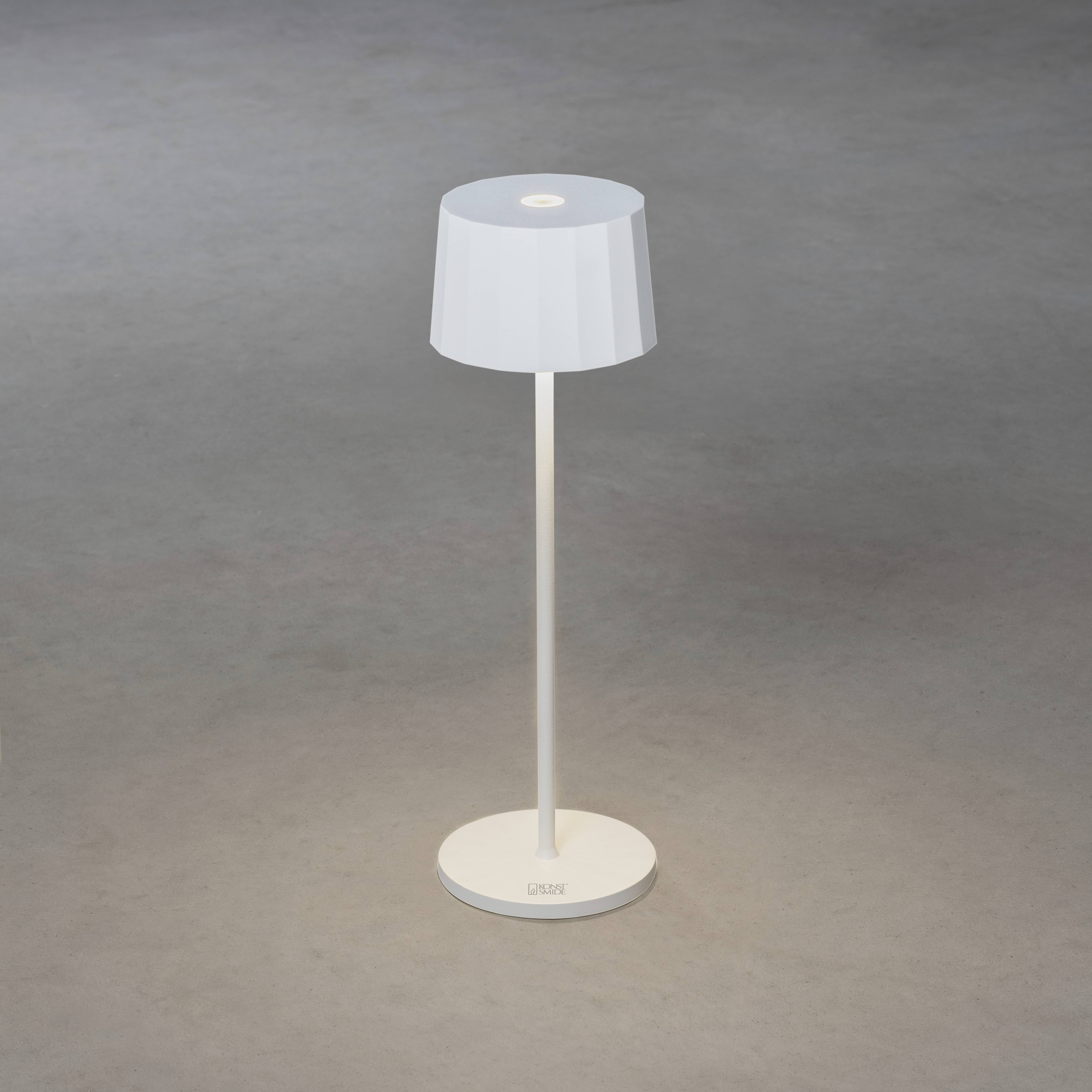 Eine weiße Tischlampe mit einem schlanken Ständer und einem runden Schirm steht auf einem grauen Boden.