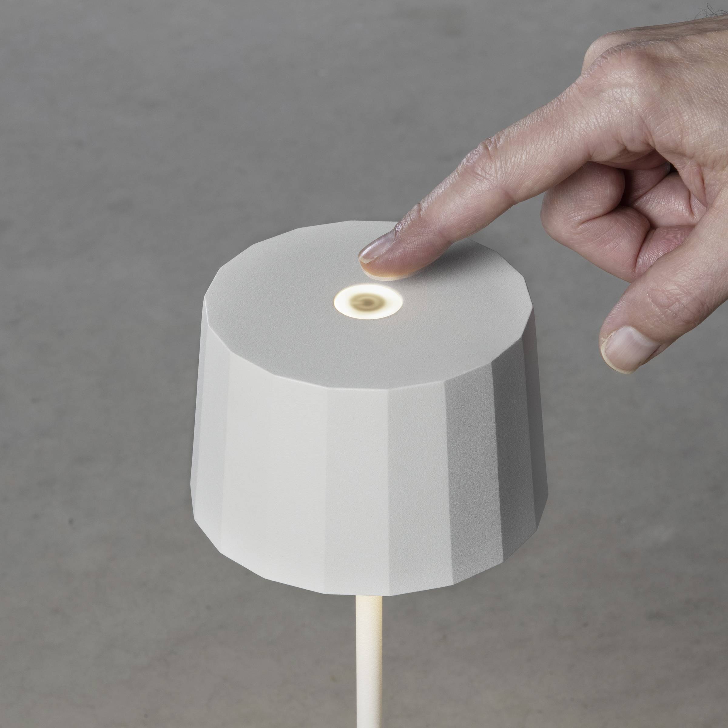 Eine Hand berührt eine minimalistische Lampe mit einem achteckigen Schirm, was die Lampe einschaltet.