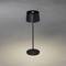 Eine schwarze Steh- oder Tischlampe beleuchtet den grauen Boden, umgeben von Schatten. Die Lampe hat einen runden Schirm und Sockel.