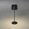 Eine schwarze Stehlampe mit rundem Schirm steht auf grauem Boden. Sie beleuchtet den Boden darunter.