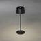 Eine moderne schwarze Tischlampe mit zylindrischem Schirm beleuchtet den grauen Boden von oben.