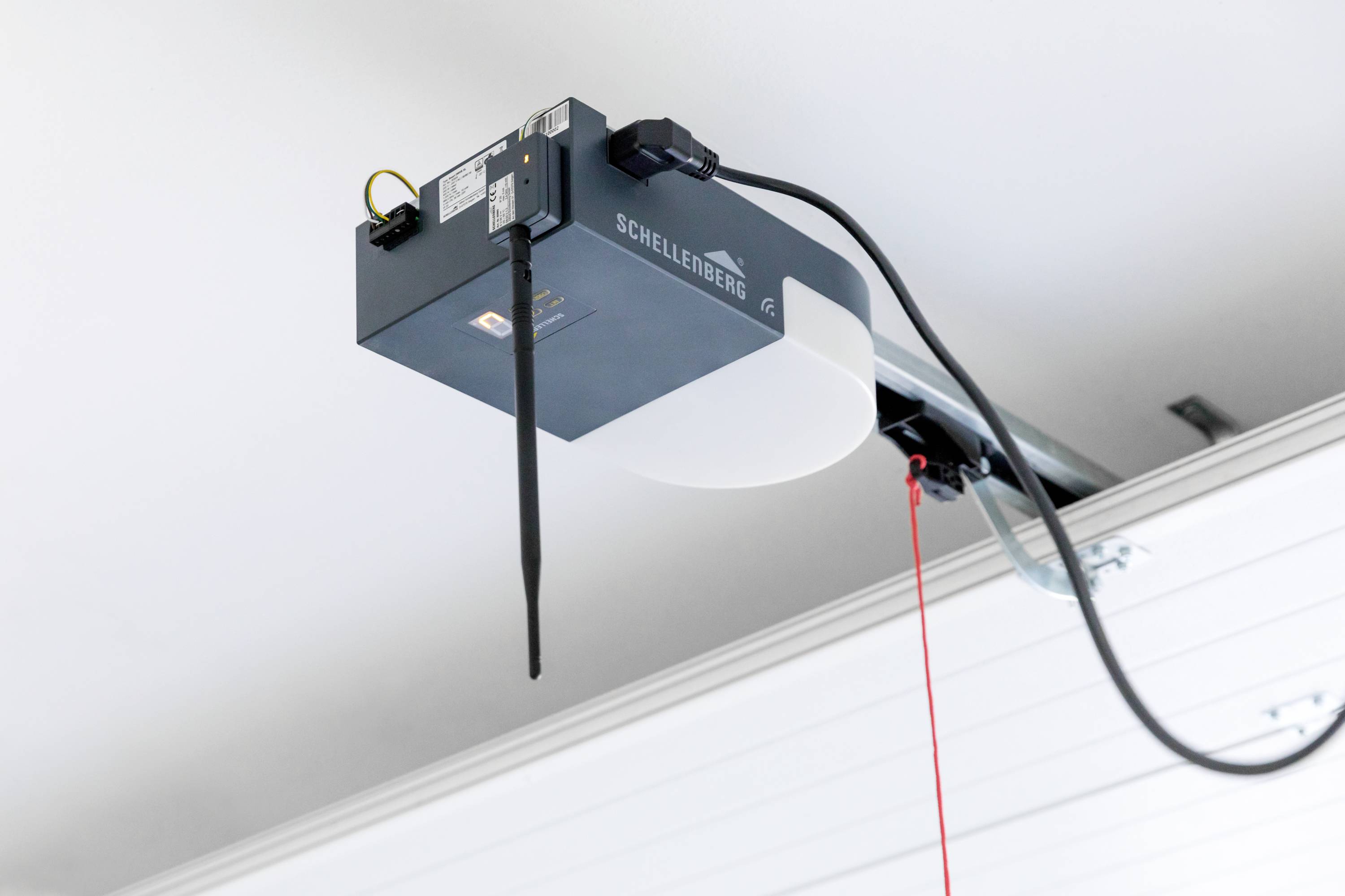 Garagenöffnungssystem an der Decke mit roten Kabelzug, Antenne und Kabeln, möglicherweise zur automatischen Türöffnung.