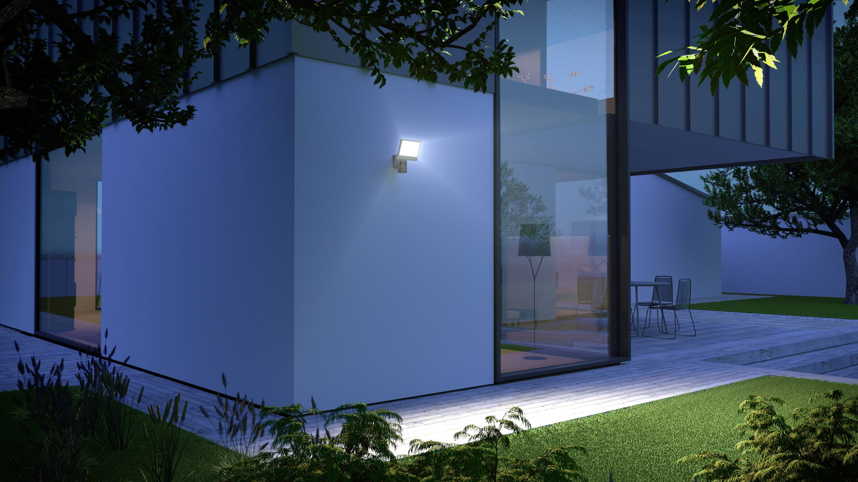 Ein modernes Haus bei Nacht mit eingeschaltetem Außenlicht. Große Glasfenster geben den Blick auf den beleuchteten Innenraum frei.