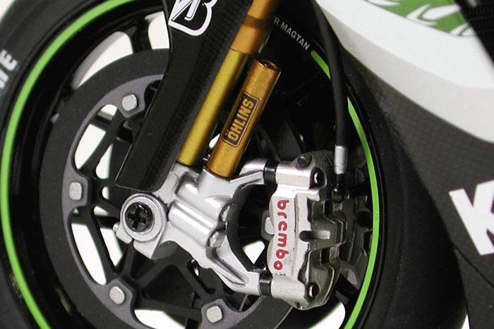 Nahaufnahme eines Motorradbremssystems mit Brembo-Bremssattel und Öhlins-Federbeinen. Das Rad hat grüne Streifen auf dem Reifen.