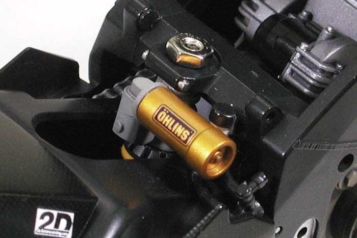 Ein Stoßdämpfer in einem Motorrad, goldfarben mit dem Markennamen 'Öhlins'. Der Stoßdämpfer ist an einem schwarz lackierten Rahmen montiert.