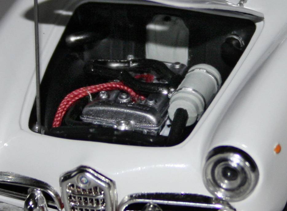 Motorraum eines Autos mit sichtbarem Motor und Kabeln, Fokus auf rote Verkabelung und silberne Motorteile unter geöffneter Motorhaube.