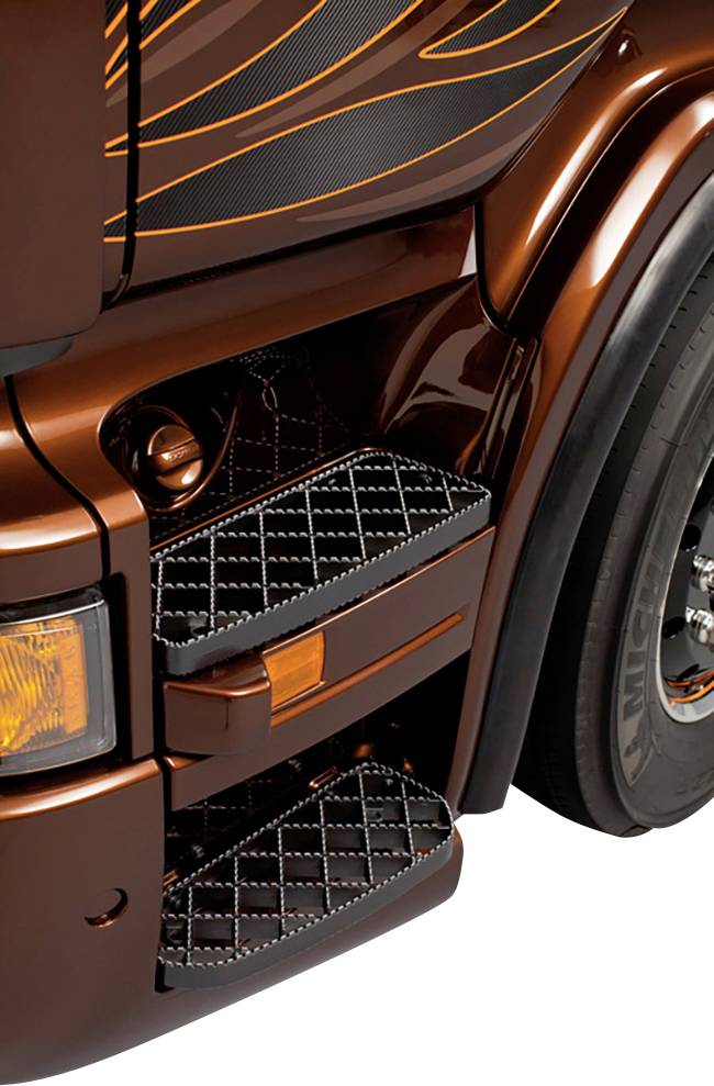 Detailaufnahme der braunen Fahrerkabine eines Lastwagens mit stilvollen schwarzen Trittbrettern und einem Reifen im Hintergrund.