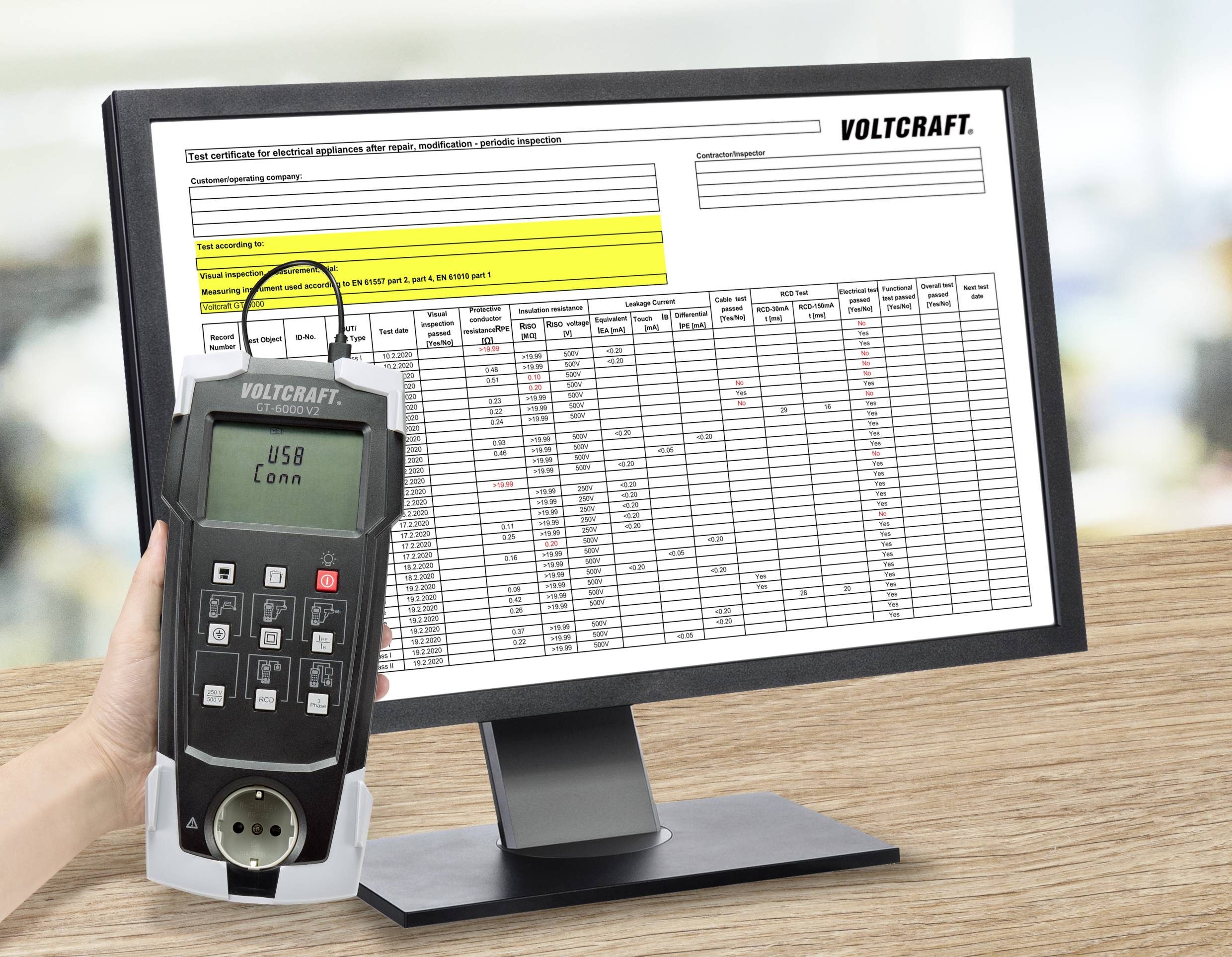 Eine Hand hält ein Voltcraft-Messgerät vor einem Computerbildschirm, der eine Tabelle mit Messwerten und technischen Daten anzeigt.