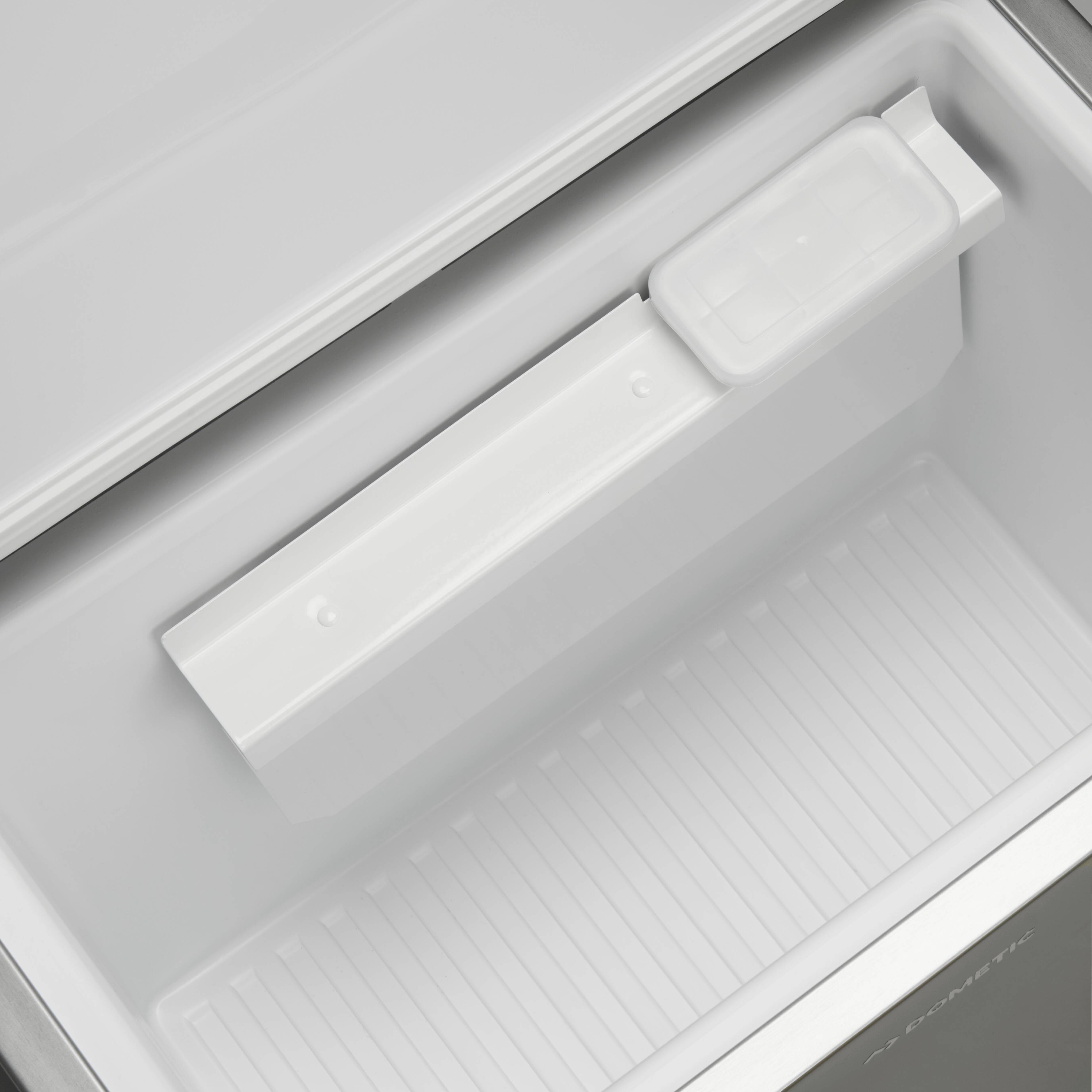 Ein leerer, geöffneter Gefrierschrank mit sichtbar herausnehmbarem Eiswürfelbehälter, der oben am oberen Rand angebracht ist.
