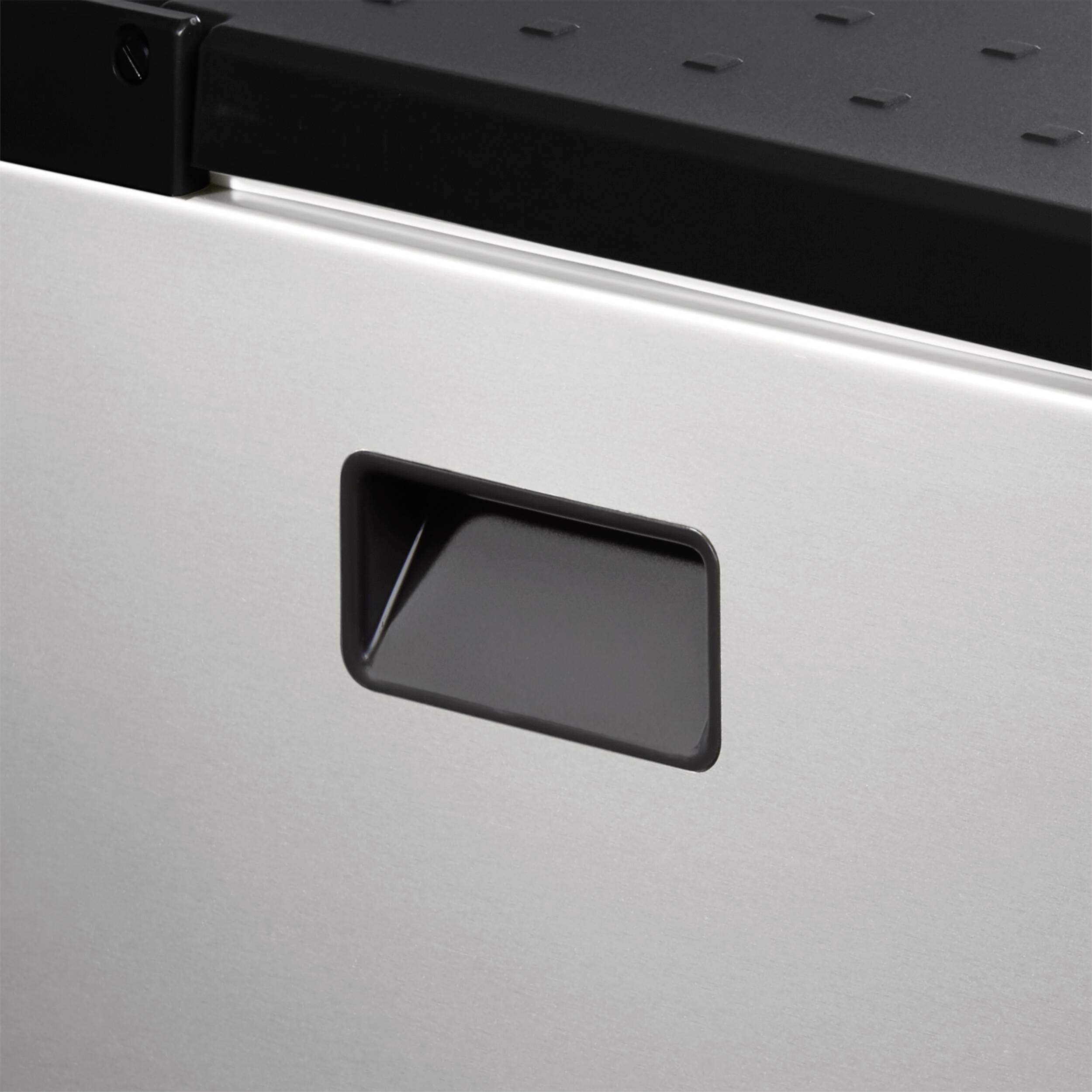 Ein silberfarbener Schrank mit schwarzem Griff an der Vorderseite. Die Oberfläche oben ist schwarz und hat kleine Einkerbungen.