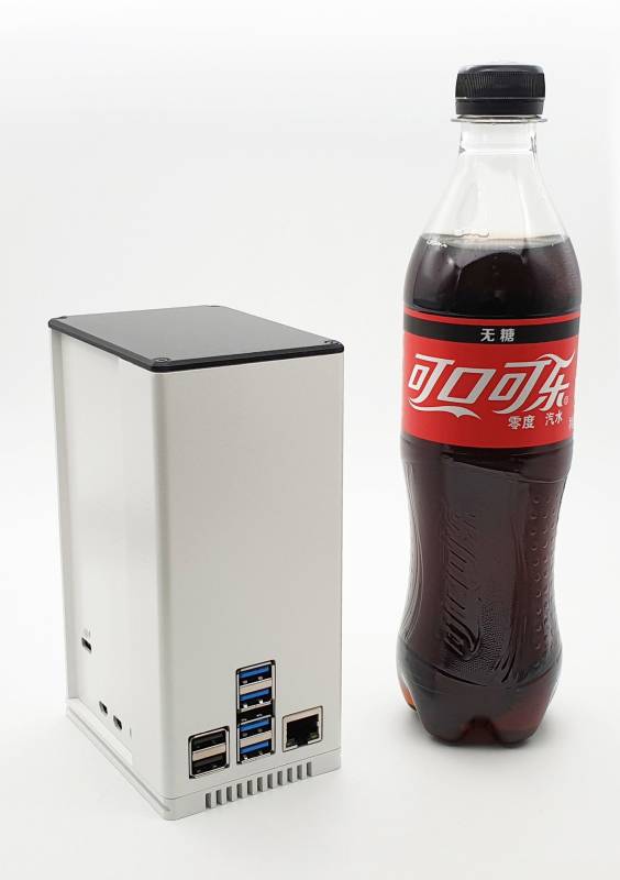 'Ein grauer, turmartiger Mini-PC steht aufrecht neben einer 500-ml-Flasche Cola, um die kompakte Größe des PCs zu verdeutlichen.'