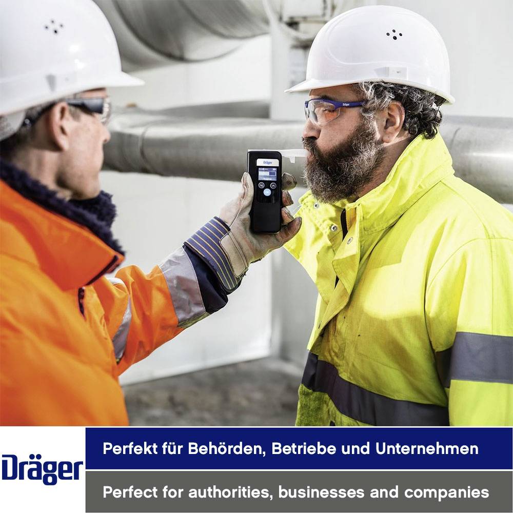 Zwei Personen in Arbeitskleidung. Eine hält ein Messgerät vor das Gesicht der anderen Person. Firmenlogo: 'Dräger'.