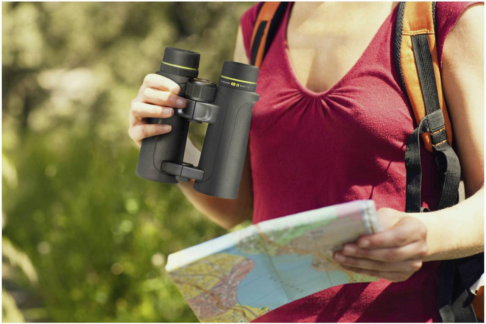 Eine Person trägt einen Rucksack und hält ein Fernglas sowie eine Karte, bereit für eine Wanderung oder Erkundung im Freien.