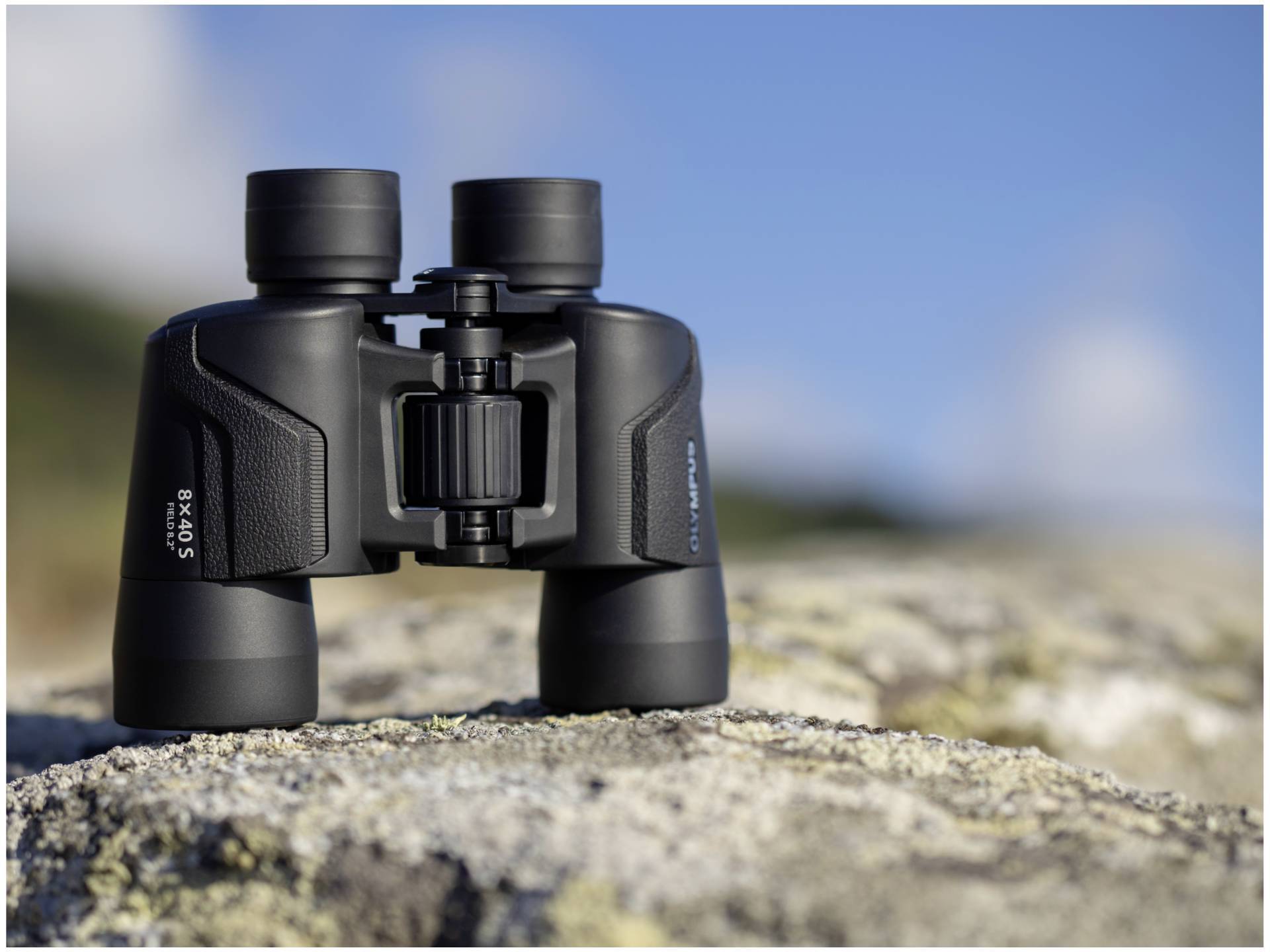 Ein Fernglas liegt auf einem Felsen vor einem unscharfen Hintergrund bei klarem Himmel, bereit für die Beobachtung von Landschaften.