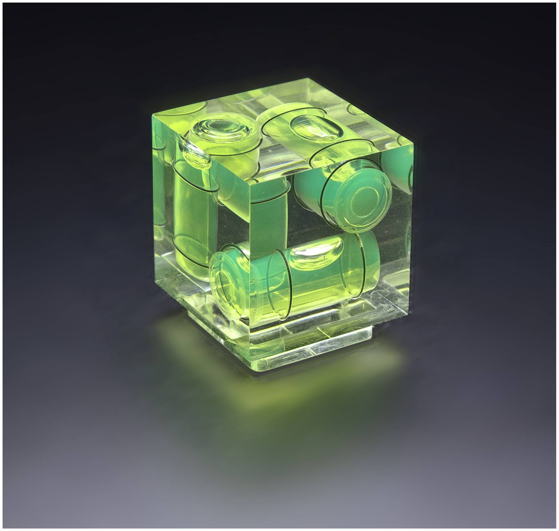Ein transparent-grüner Würfel mit eingeschlossenen zylindrischen Formen steht auf einer dunklen Oberfläche und spiegelt Licht wider.