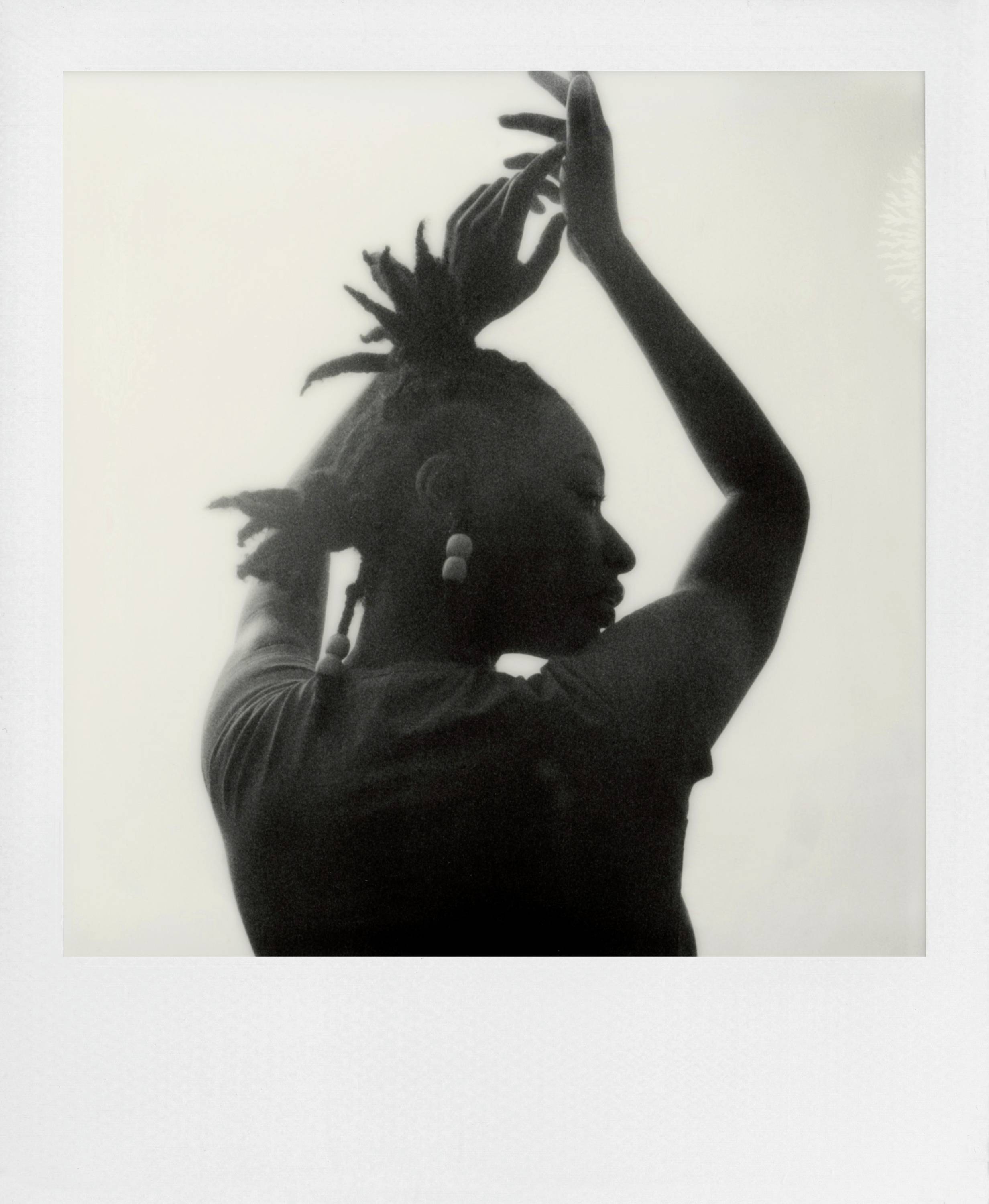 Silhouette einer Person mit hoch erhobenen Armen, seitliche Ansicht; die Haare in einem stilvollen Muster hochgesteckt.