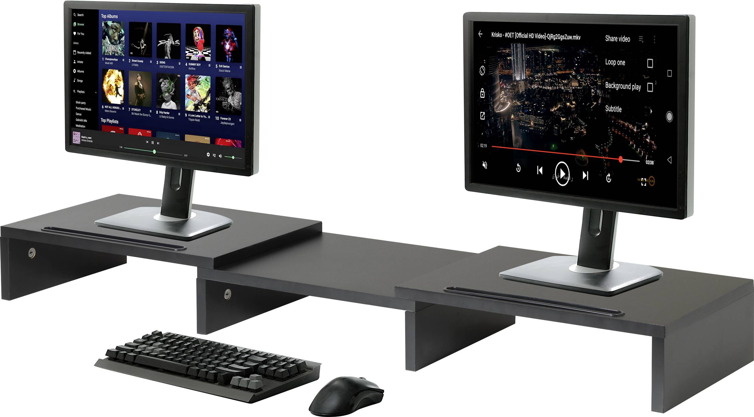 Zwei Computermonitore nebeneinander auf erhöhten Plattformen; der linke zeigt Musikstreaming, der rechte ein Video mit Stadtansicht. Darunter: Tastatur und Maus.