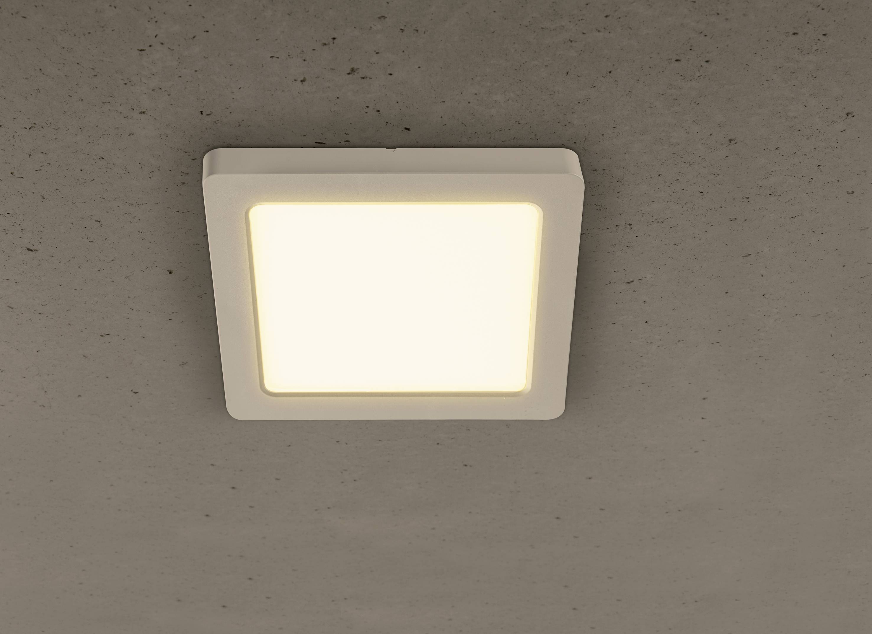 Weiße, quadratische Deckenlampe leuchtet auf einer grauen Zimmerdecke.