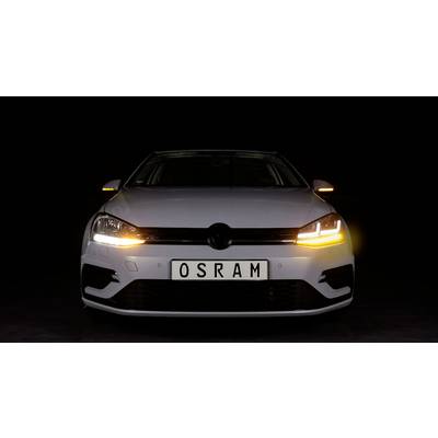 Ein weißes Auto mit leuchtenden Scheinwerfern und einem Nummernschild mit der Aufschrift 'OSRAM' steht vor einem dunklen Hintergrund.