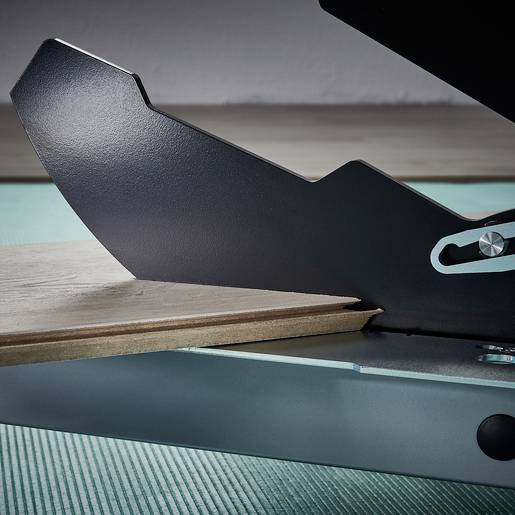 Nahaufnahme einer Schneidemaschine auf einem Tisch mit einem Holzstück darunter, zeigt die Klinge und den Mechanismus der Maschine.