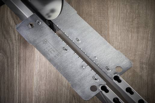 Metallteil mit Zahnrad und Löchern auf Holzoberfläche. Werkzeug oder Bauelement, möglicherweise für Montage oder Befestigung.