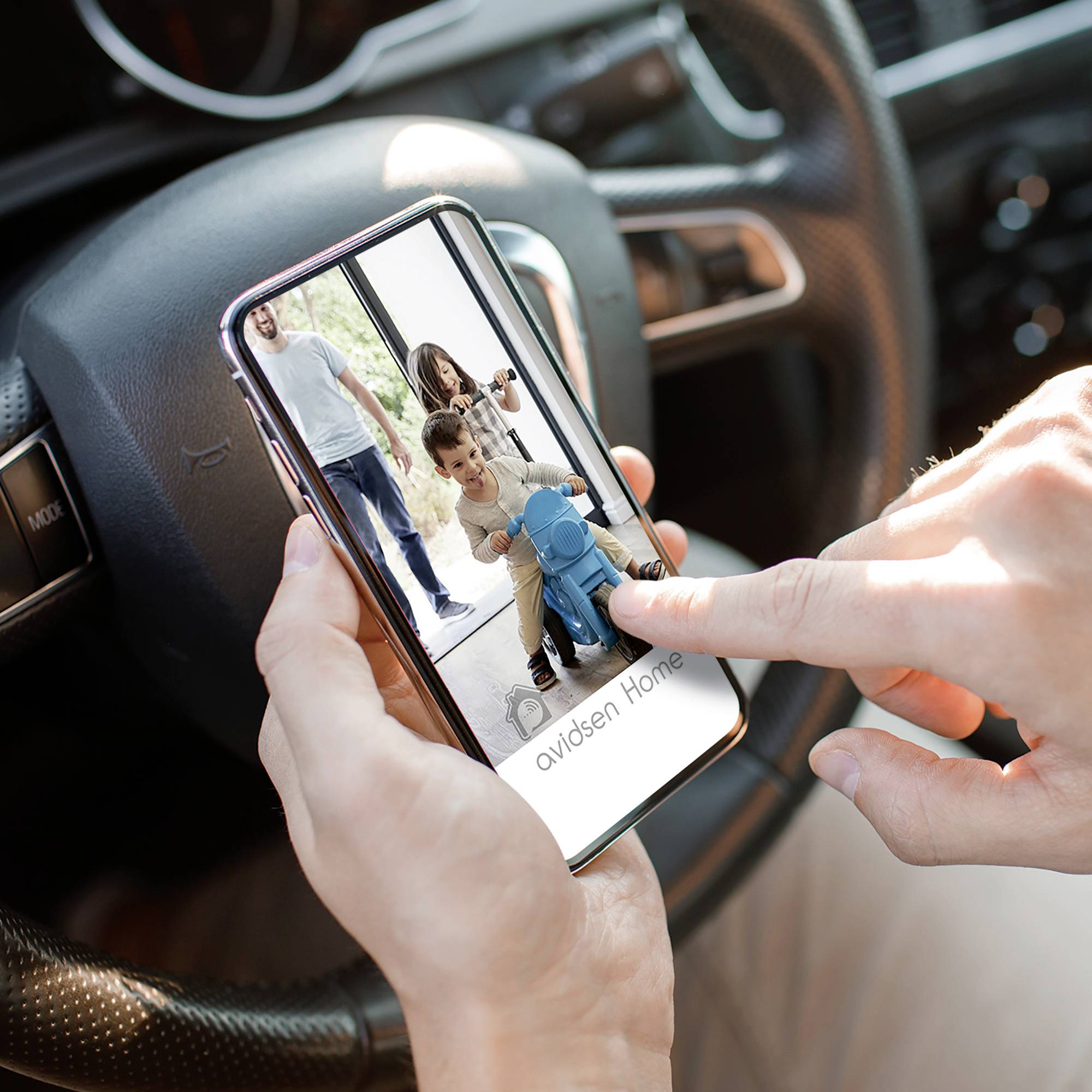 Eine Person hält ein Smartphone in einem Auto. Auf dem Bildschirm ist ein Bild von zwei Kindern zu sehen, die mit einem Spielzeug spielen.