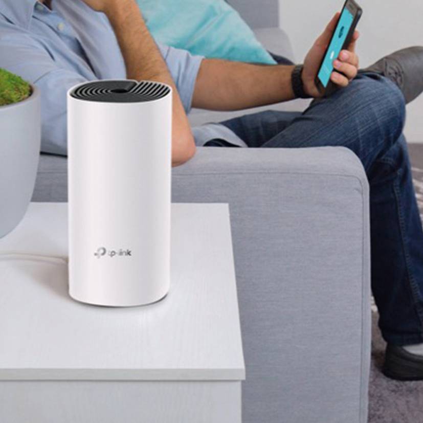 Eine Person sitzt auf einem Sofa und benutzt ein Smartphone. Auf dem Tisch steht ein weißer WLAN-Router.