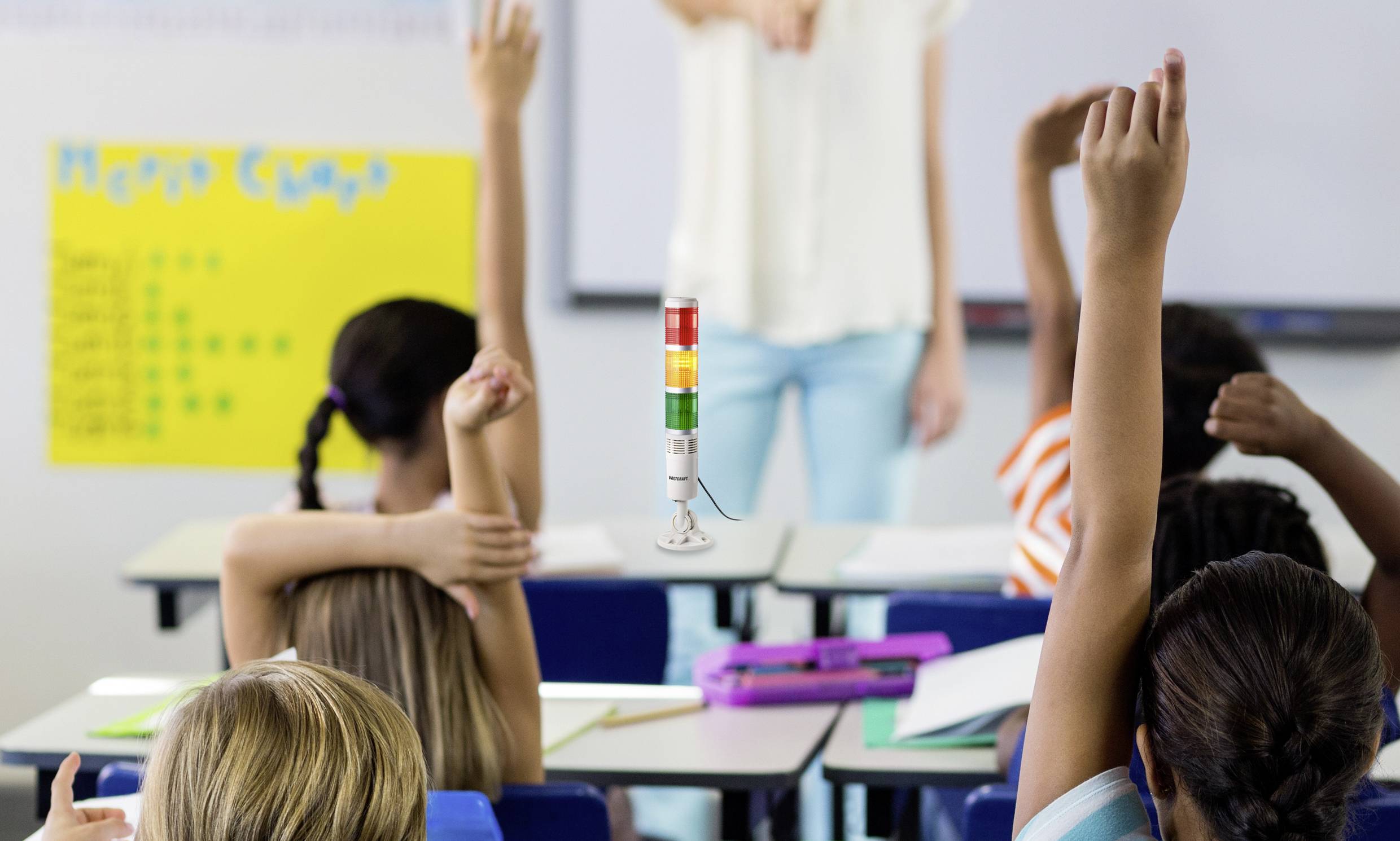 Kinder heben die Hände im Klassenzimmer, um sich zu melden. Im Vordergrund ein Ampelsystem, das den Lärmpegel anzeigt.