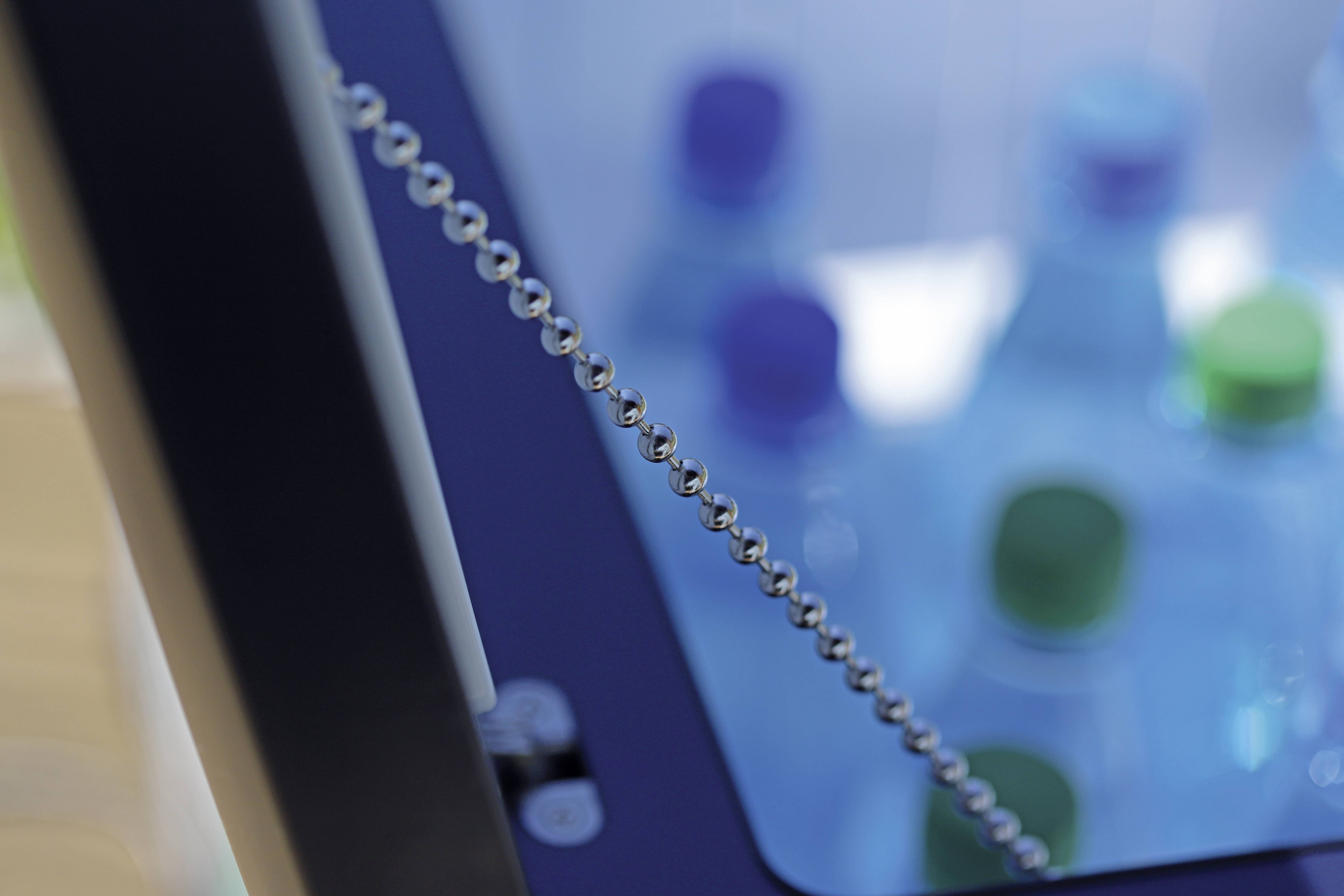 Ein Getränkeautomat mit mehreren Wasserflaschen im Inneren, die mit verschiedenfarbigen Deckeln verschlossen sind. Im Vordergrund ist die Kette der Automatenklappe sichtbar.