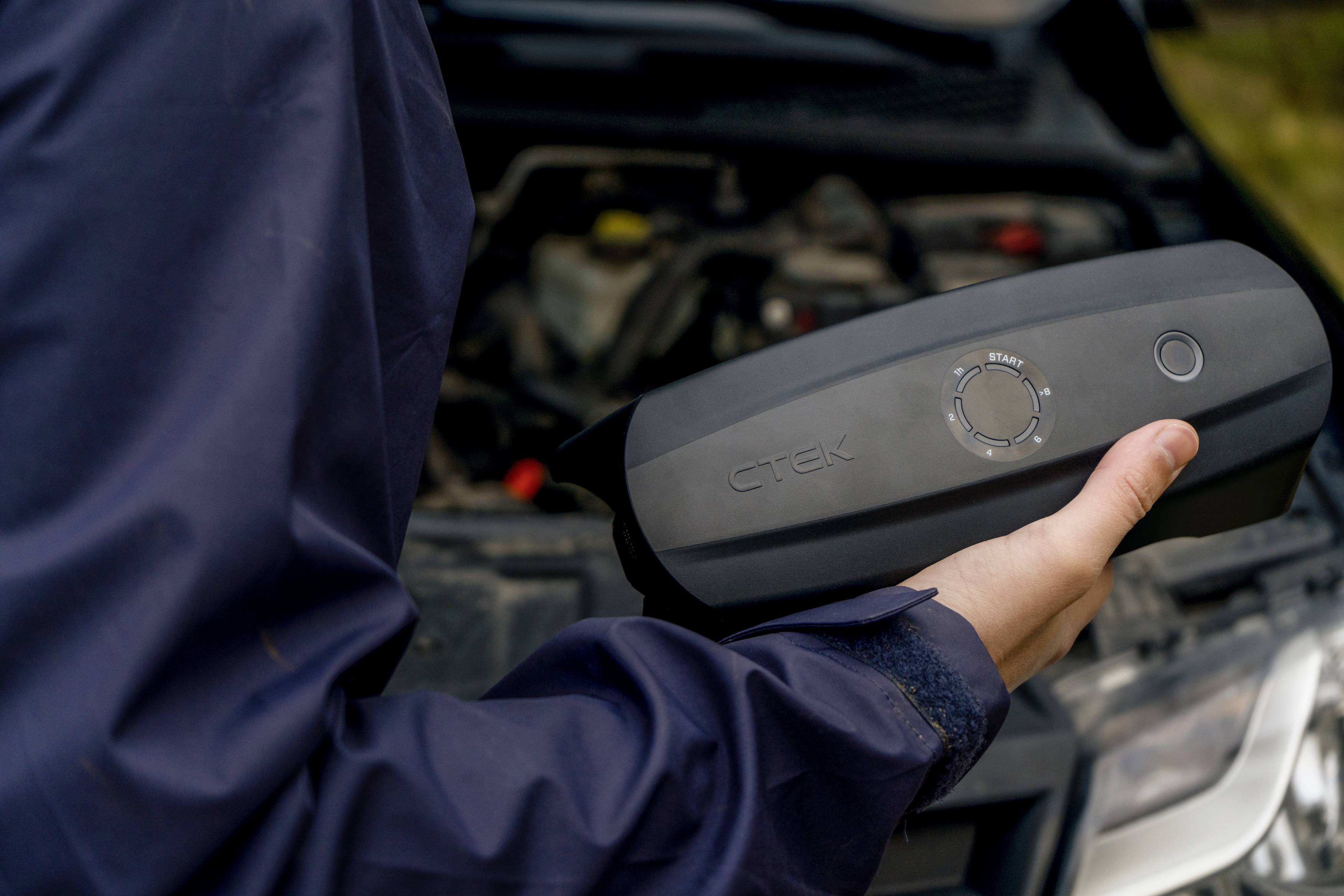 Eine Person hält ein batteriebetriebenes Gerät vor einem geöffneten Auto. Das Gerät zeigt einen Ladezustand an.