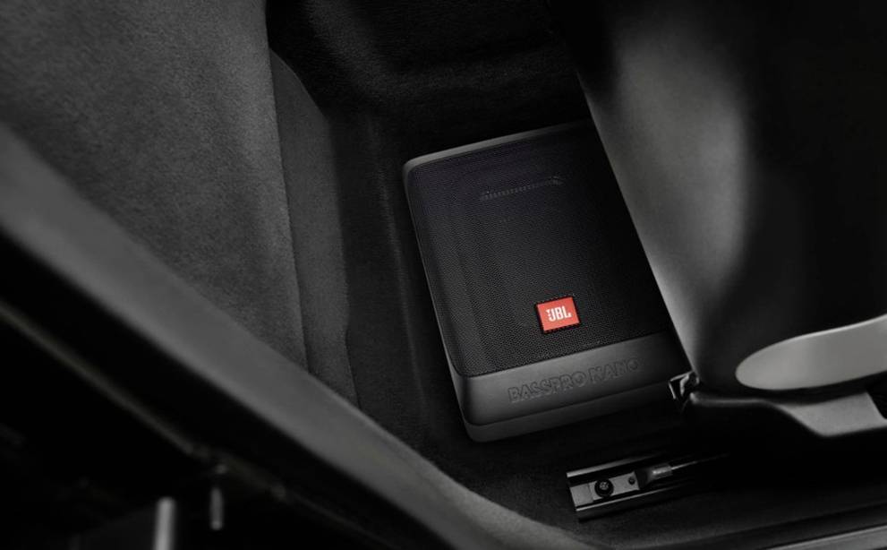 Subwoofer in einem Fahrzeugkofferraum, mit rotem 'JBL'-Logo. Der Subwoofer ist in einer schwarzen, gepolsterten Umgebung eingebaut.
