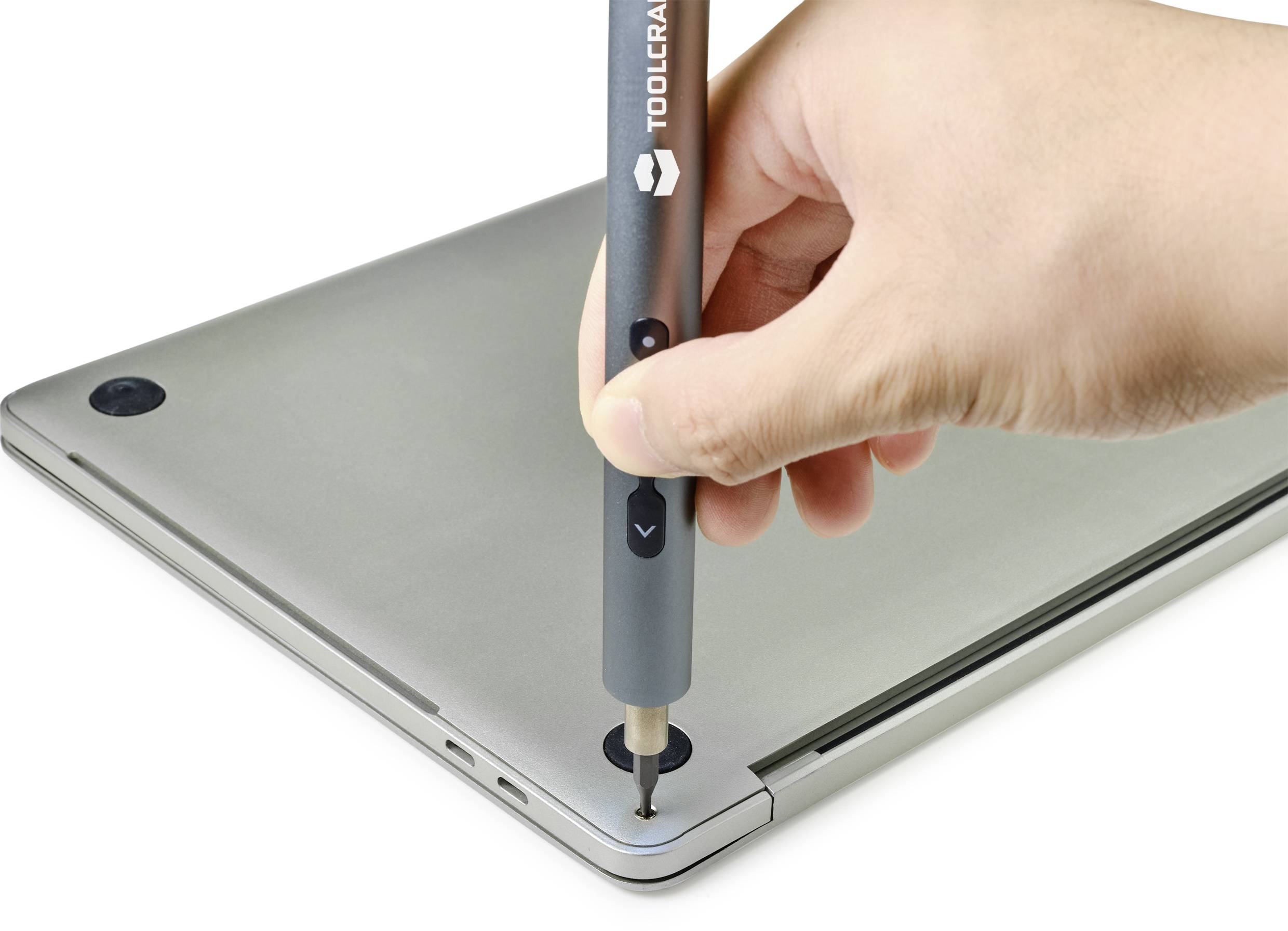 Eine Hand hält einen Schraubendreher, um eine Schraube an einem Laptop-Gehäuse zu entfernen.