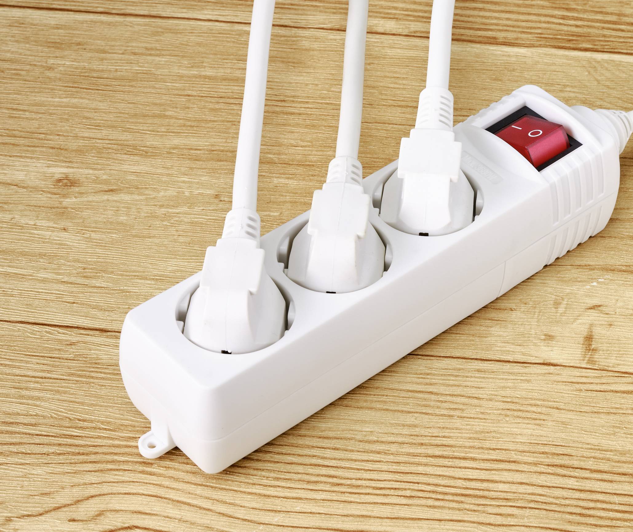 Mehrfachsteckdose mit drei eingesteckten Kabeln und einem roten Ein-/Ausschalter auf einem Holztisch.