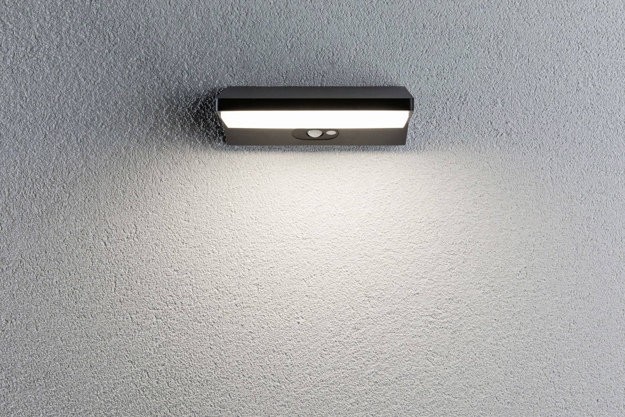 Wandleuchte mit Bewegungssensor an einer strukturierten weißen Wand, strahlt warmes Licht nach unten.