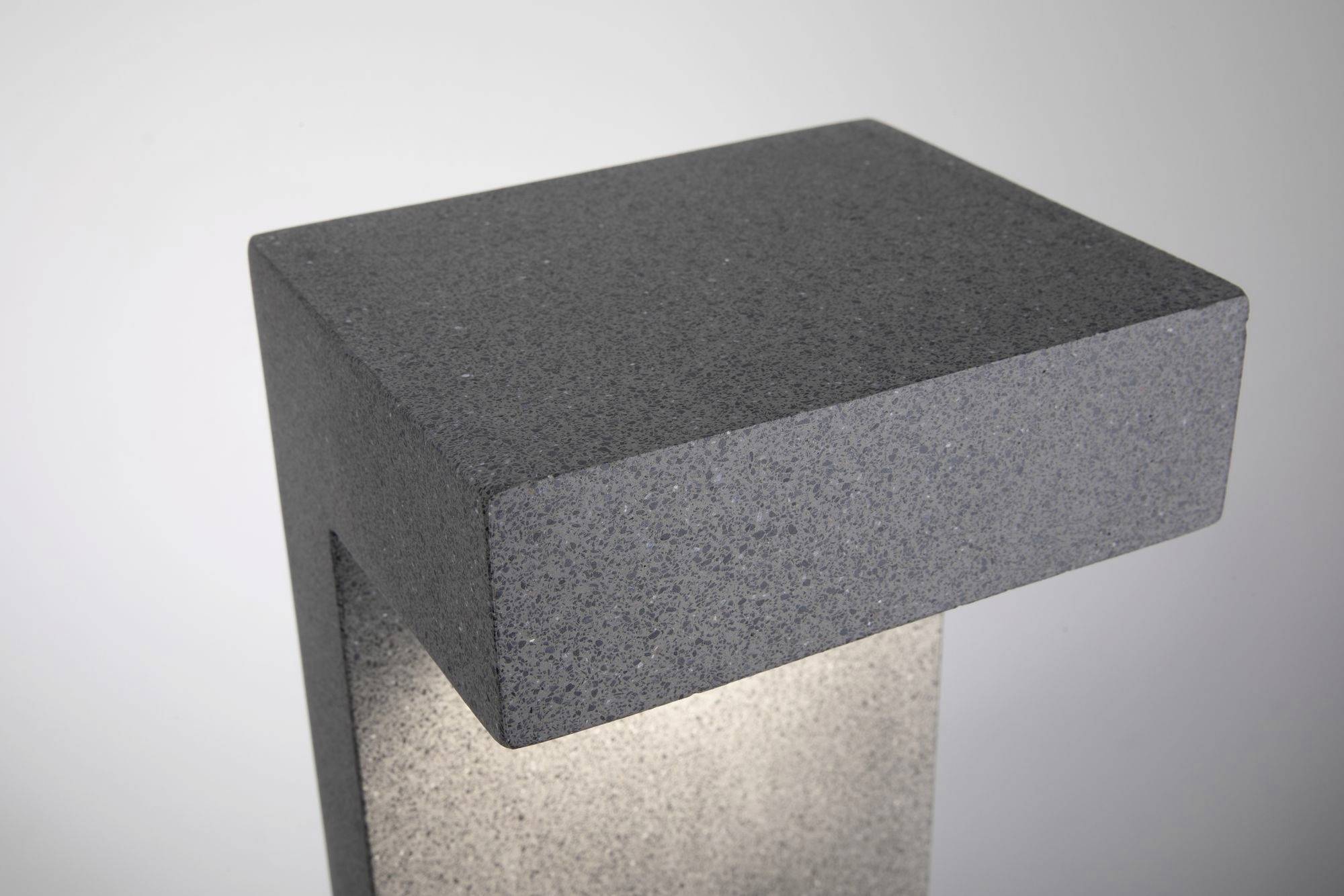 Graue betongestaltige Außenleuchte mit rechteckigem, minimalistischem Design, leuchtet nach unten, vor grauem Hintergrund.
