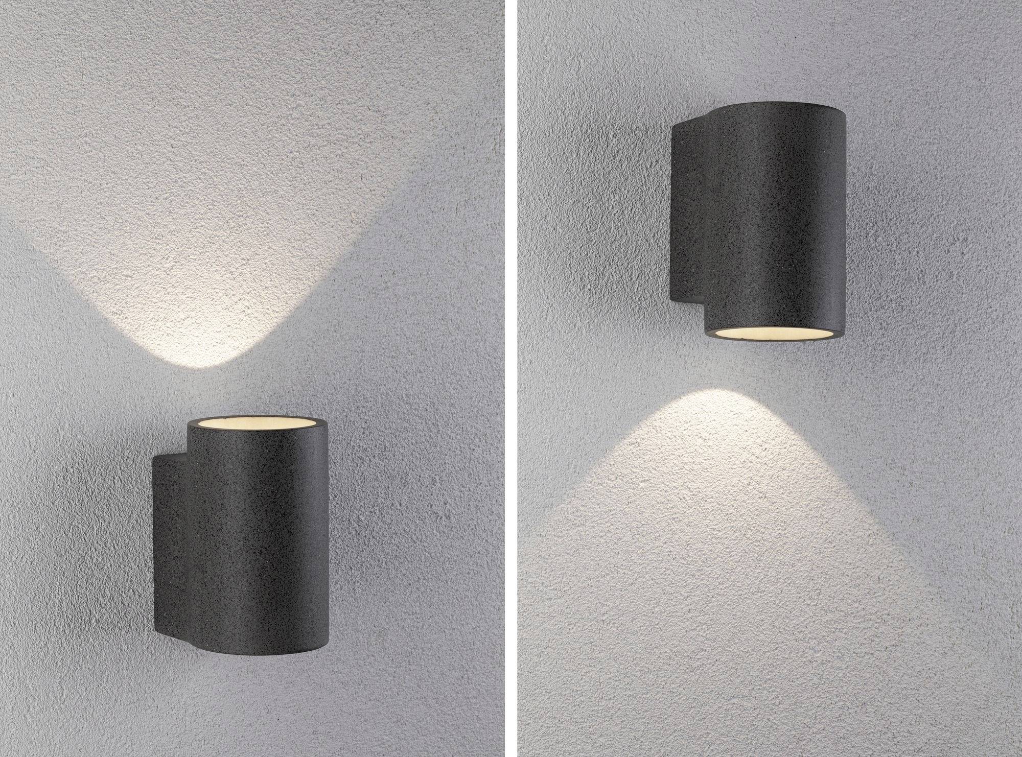Zwei Wandlampen mit modernem Design; links strahlt nach oben, rechts nach unten. Beide werfen indirektes Licht auf eine graue Wand.