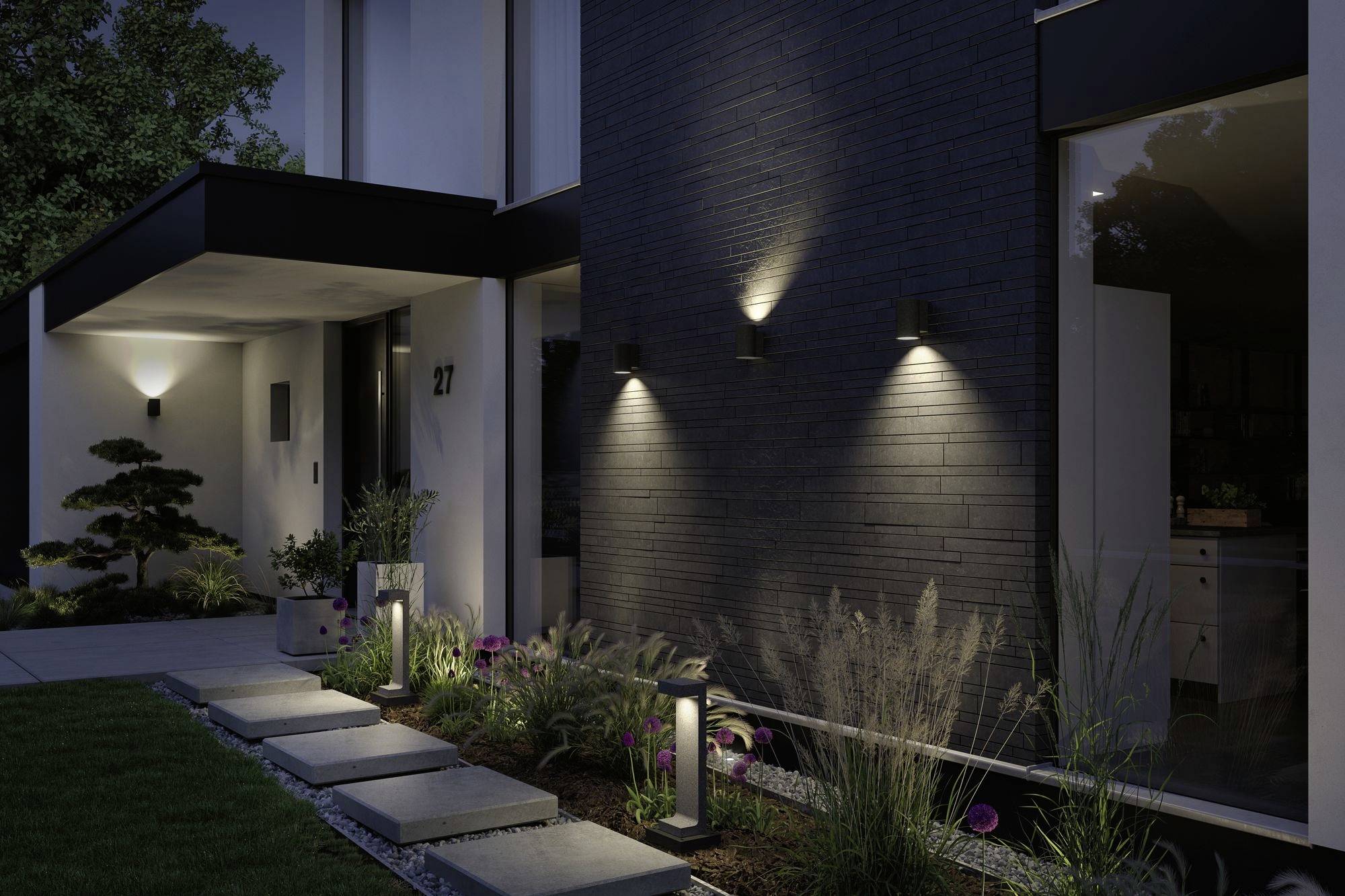 Moderne Hausfassade bei Nacht, beleuchtet durch Wandleuchten. Ein gepflegter Garten führt über Steinplatten zum Eingang.
