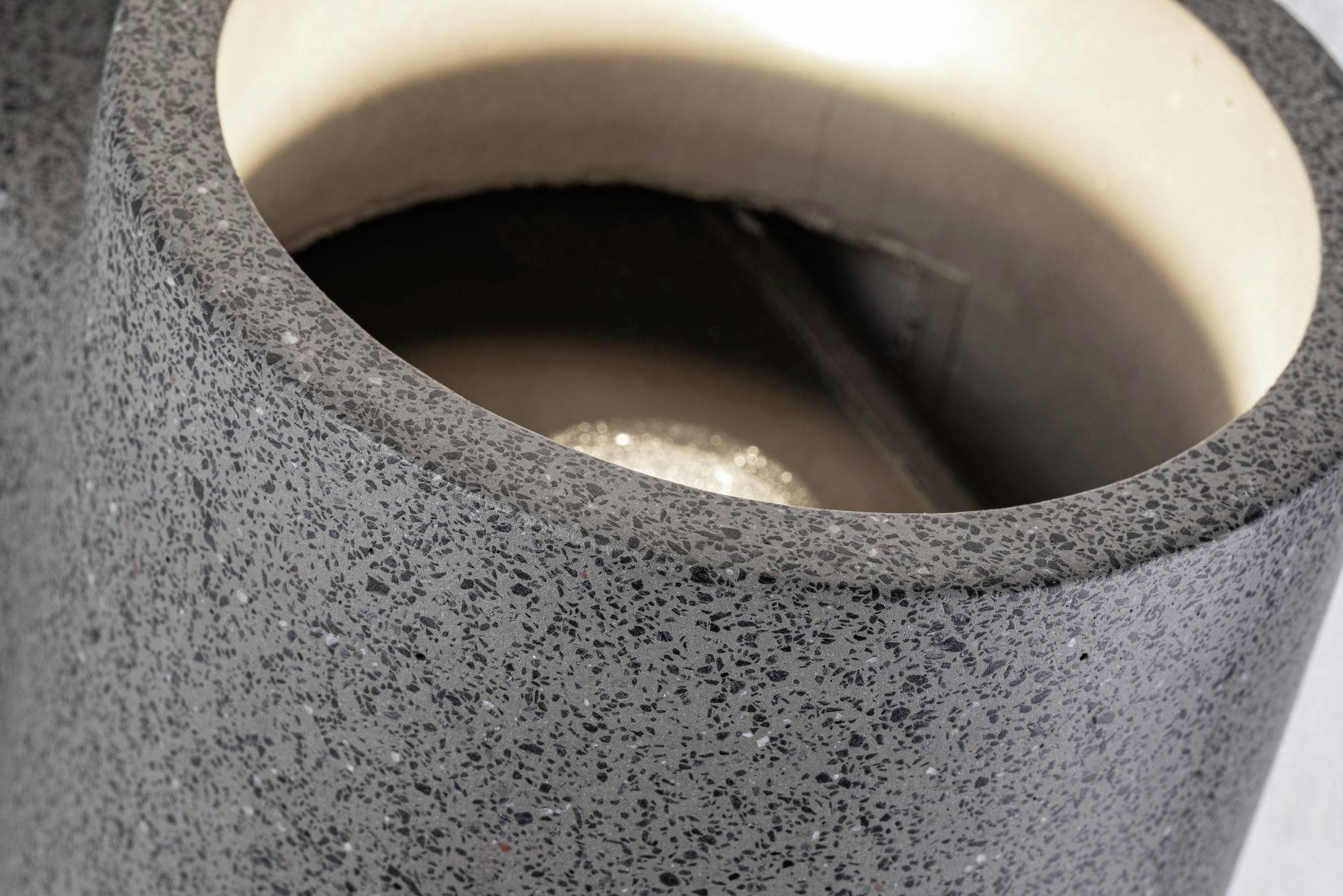 Ein moderner, zylindrischer Aschenbecher aus dunkelgrauem, strukturiertem Material mit glatter Innenfläche.