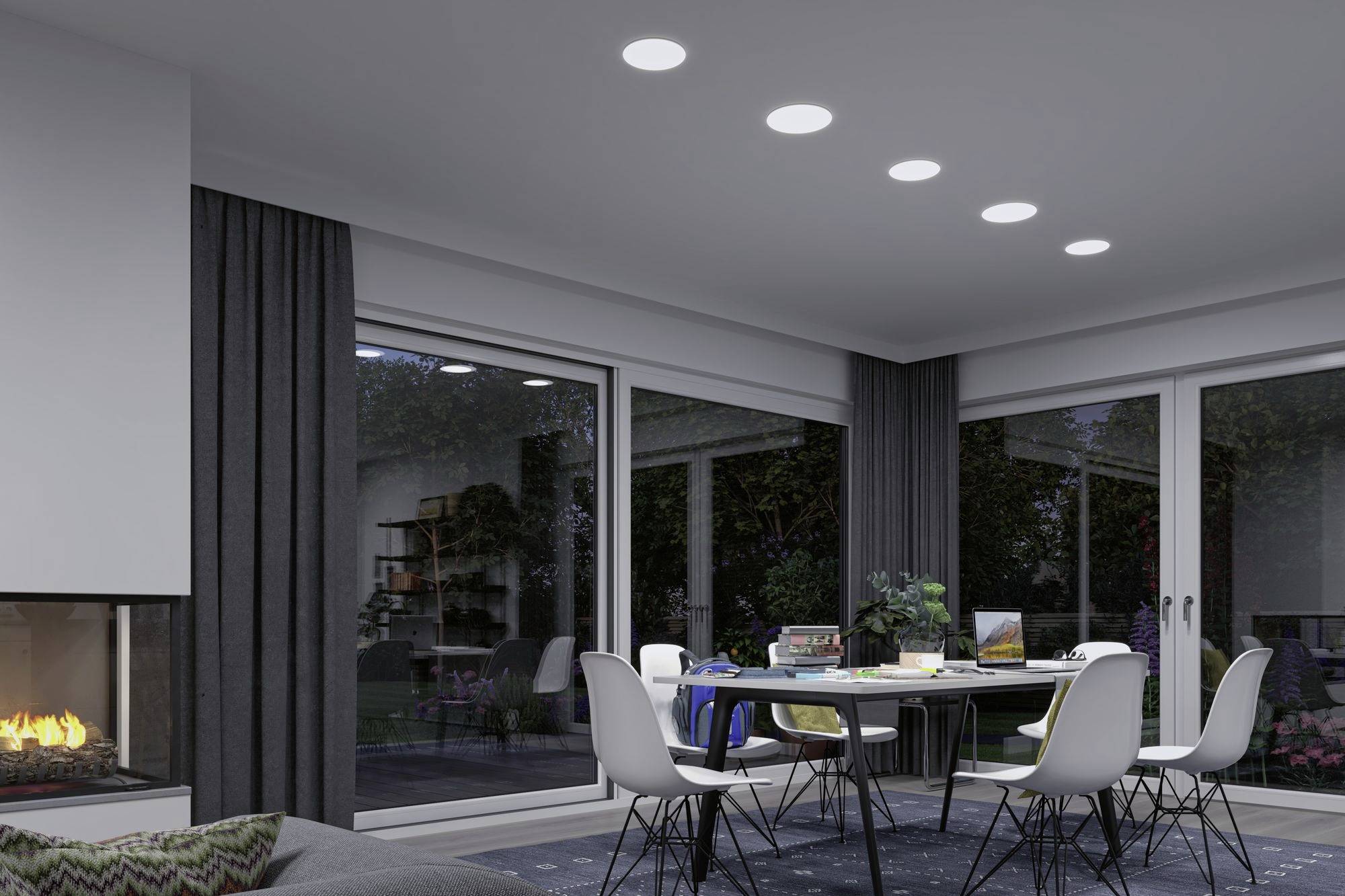 Modernes Wohnzimmer mit Esstisch und Stühlen, umgeben von großen Fenstern. Ein Kamin brennt links, über dem Tisch leuchten Deckenlichter.