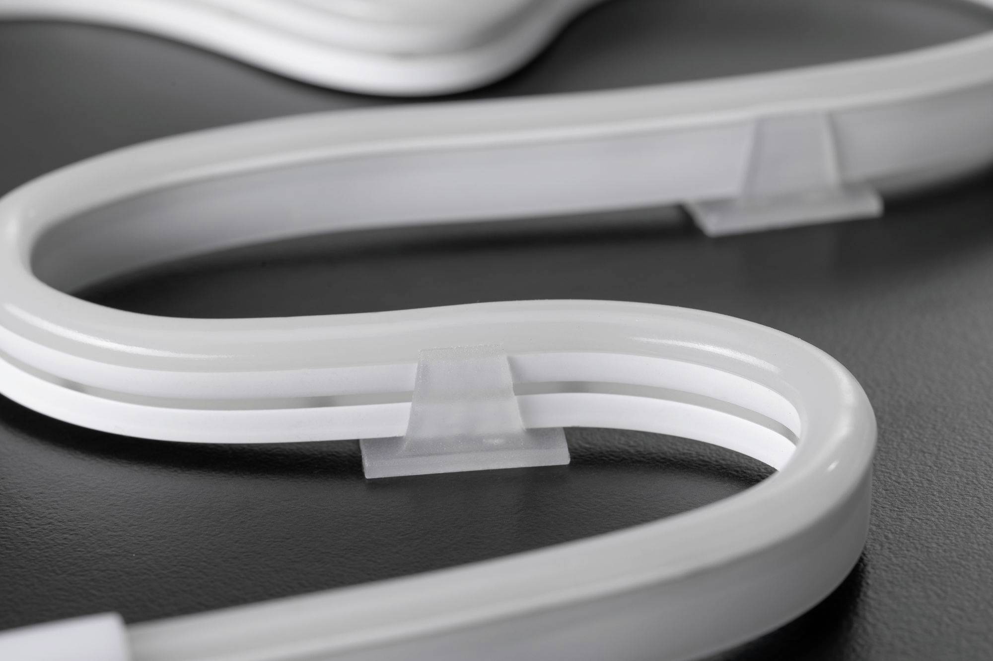 Ein gebogenes, weißes leuchtendes Objekt auf dunklem Hintergrund; es scheint ein flexibles Licht- oder Dekorationselement zu sein.