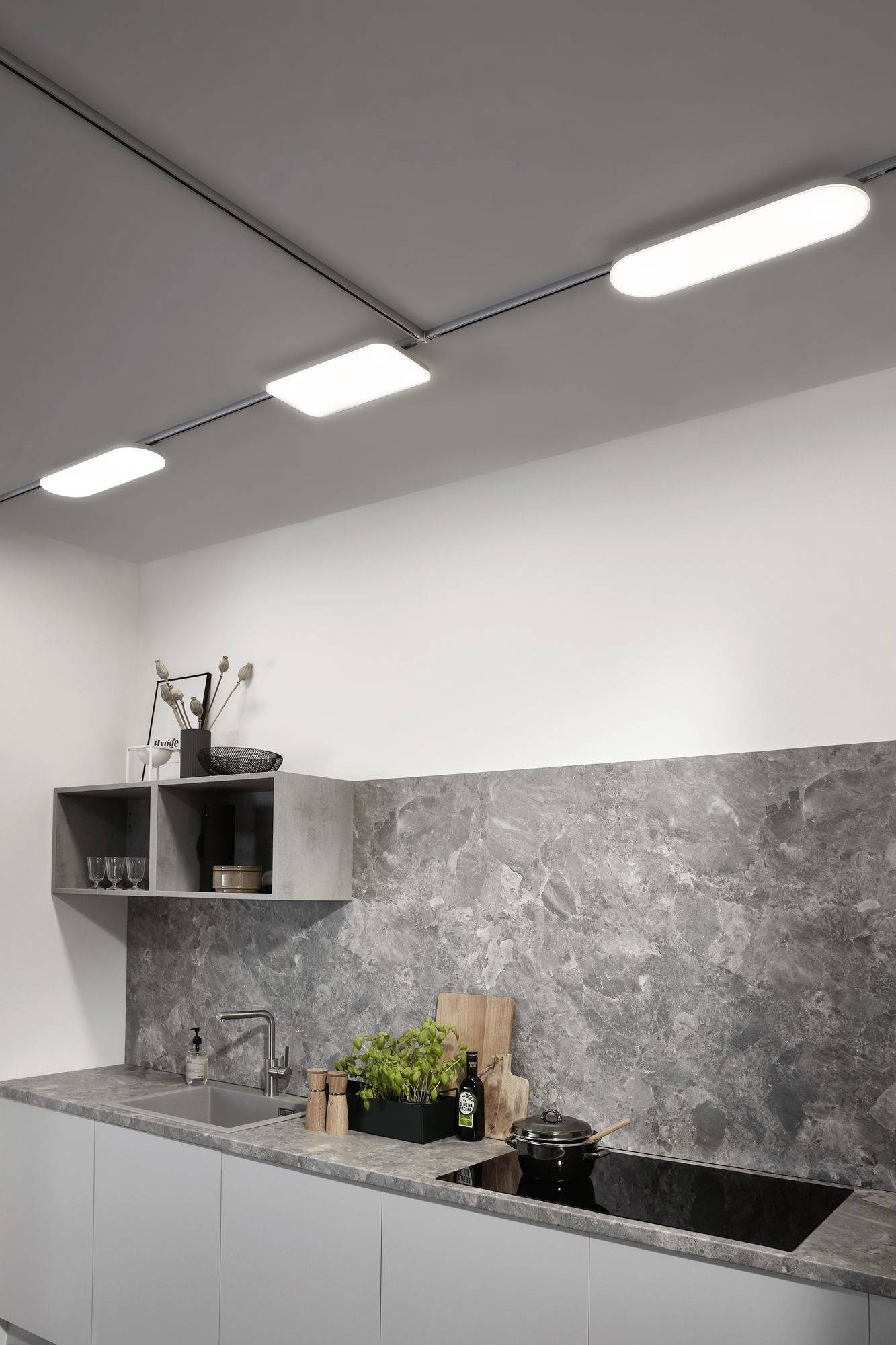 Moderne Küche mit grauem Marmorrückwand und heller Deckenbeleuchtung. Küchengeräte auf der Arbeitsplatte, Holzbrett und Kräuter.