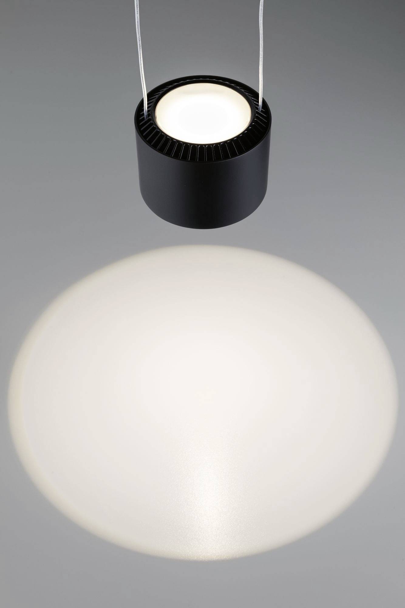 Eine einzelne, schwarze Deckenleuchte strahlt Licht nach unten und erzeugt einen großen weißen Lichtkreis auf einer grauen Fläche.