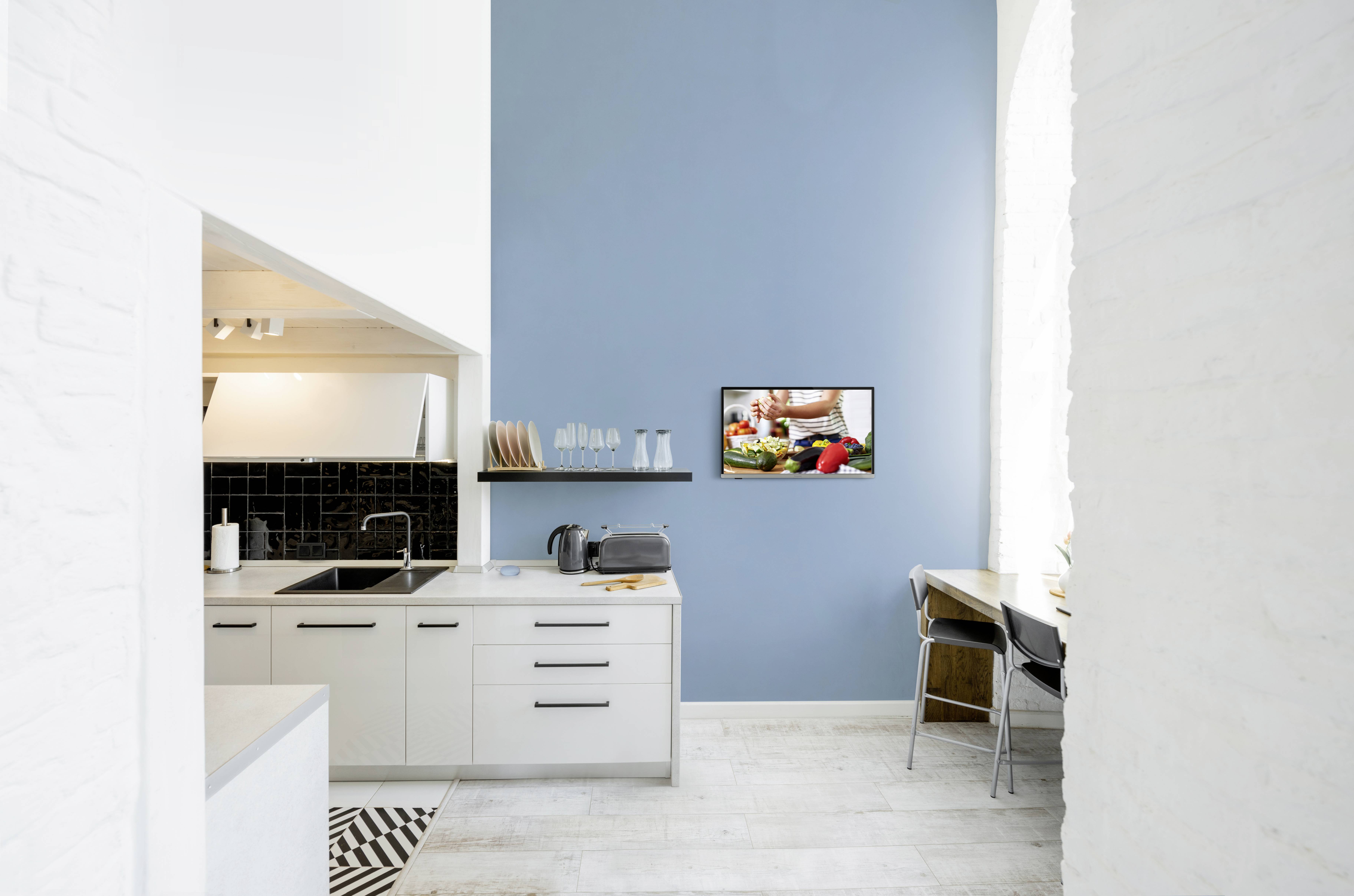 Moderne Küche mit weißem Interieur, einem blauen Wandakzent und einem Bild an der Wand, das frisches Gemüse zeigt.