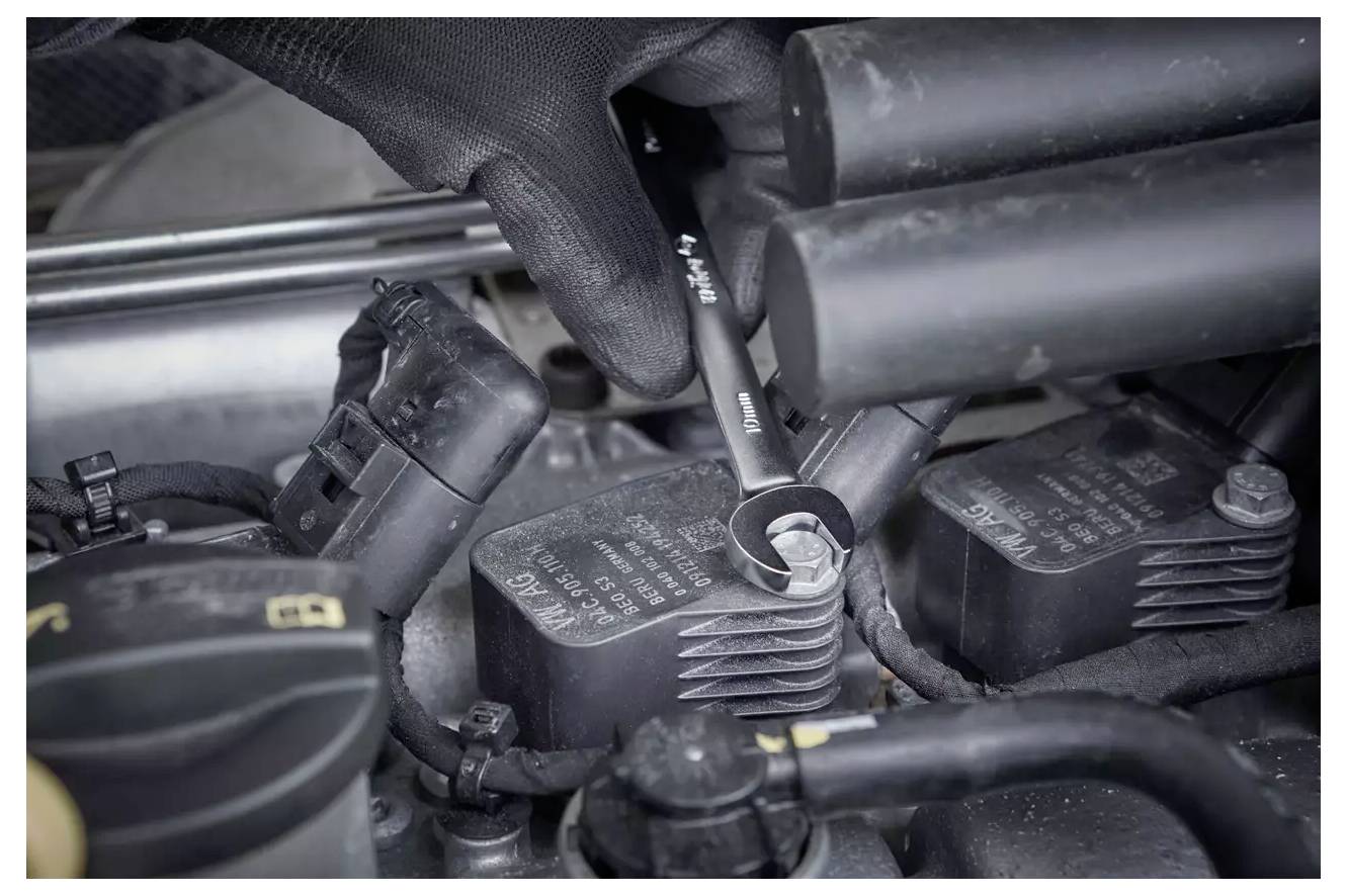 Eine Person, die einen Handschuh trägt, benutzt einen Schraubenschlüssel, um ein Bauteil in einem Automotor einzustellen und konzentriert sich dabei auf die Motorwartung oder -reparatur.