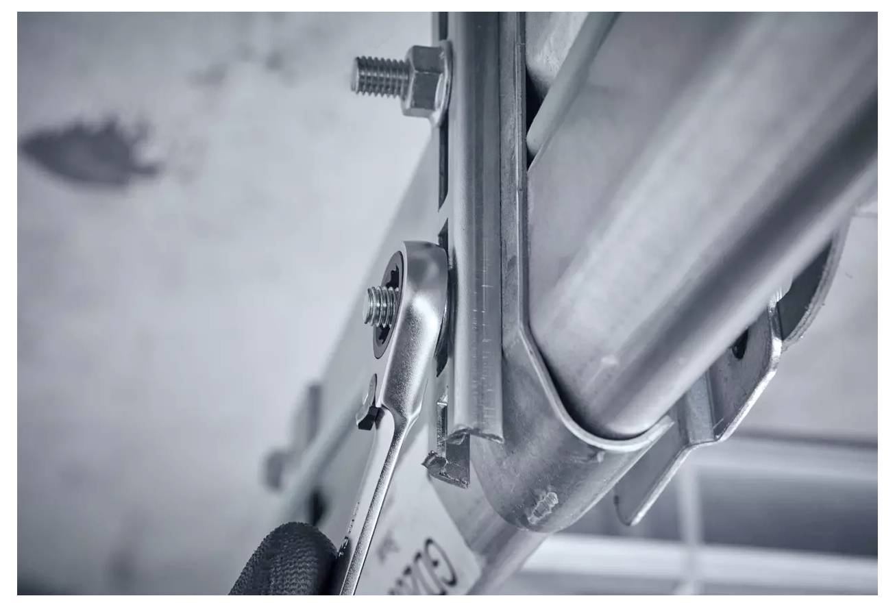 Eine Nahaufnahme einer Person, die einen Schraubenschlüssel verwendet, um eine Schraube an einem Stück Industrieausrüstung oder Gerüst festzuziehen, wobei Wartungsarbeiten dargestellt werden.