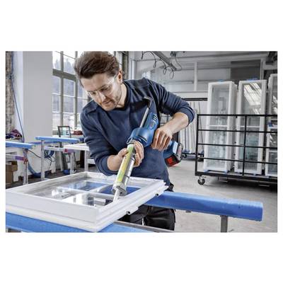 Eine Person mit Sicherheitsbrille benutzt ein Elektrowerkzeug, um einen Fensterrahmen in einer Werkstatt zu versiegeln, umgeben von Fensterpaneelen und industrieller Ausrüstung.